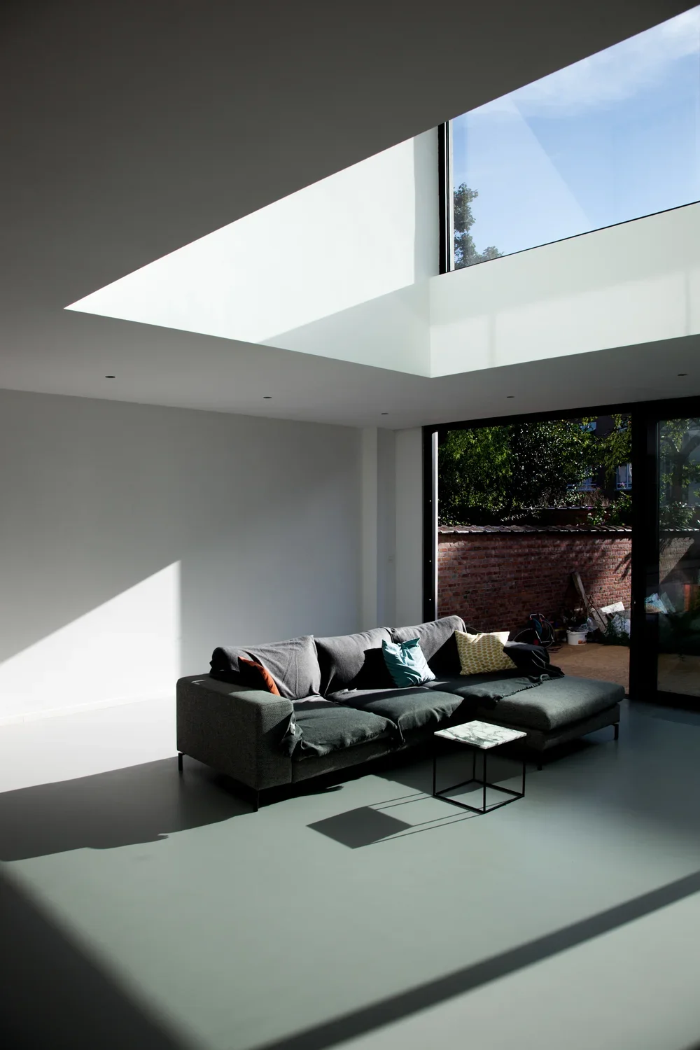 Contemporary residential living room design featuring a large custom skylight, sliding glass doors, and a seamless connection to the outdoor patio, by Tom Naeyaert Architecture.