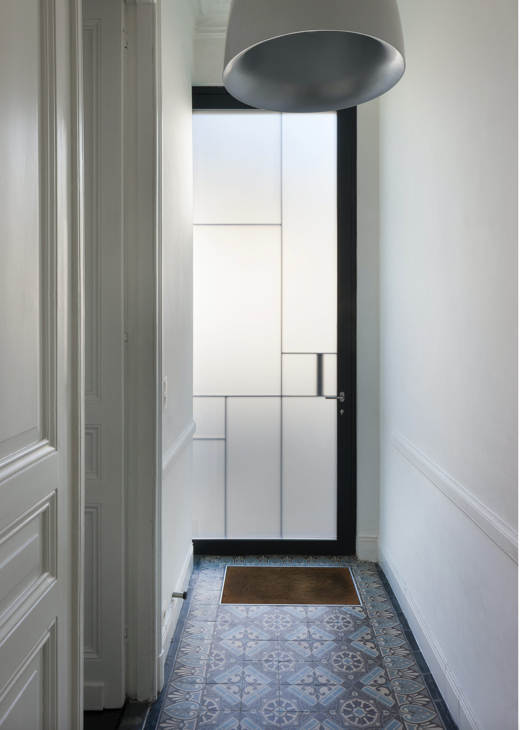 Bespoke hallway interior design featuring decorative patterned floor tiles and a modern black-framed door, by Tom Naeyaert Architecture.