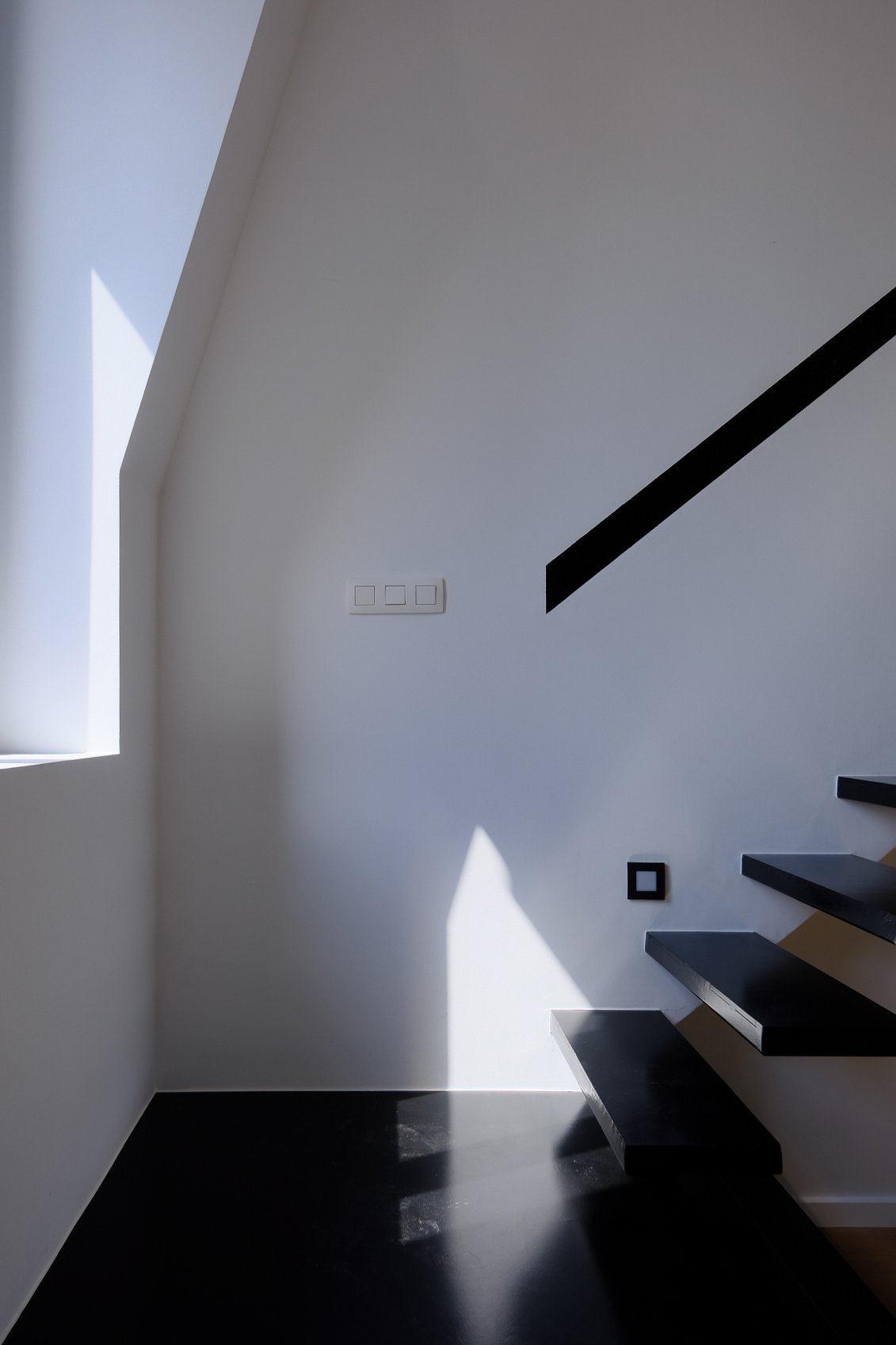 Bespoke modern staircase design with black floating steps against a white wall and a minimalist black handrail, by Tom Naeyaert Architecture.