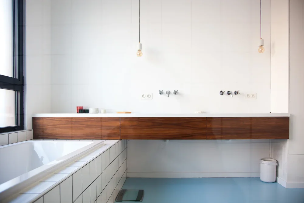 Modern bathroom with a large white bathtub, a window, a wall-mounted wooden cabinet, and minimal accessories.