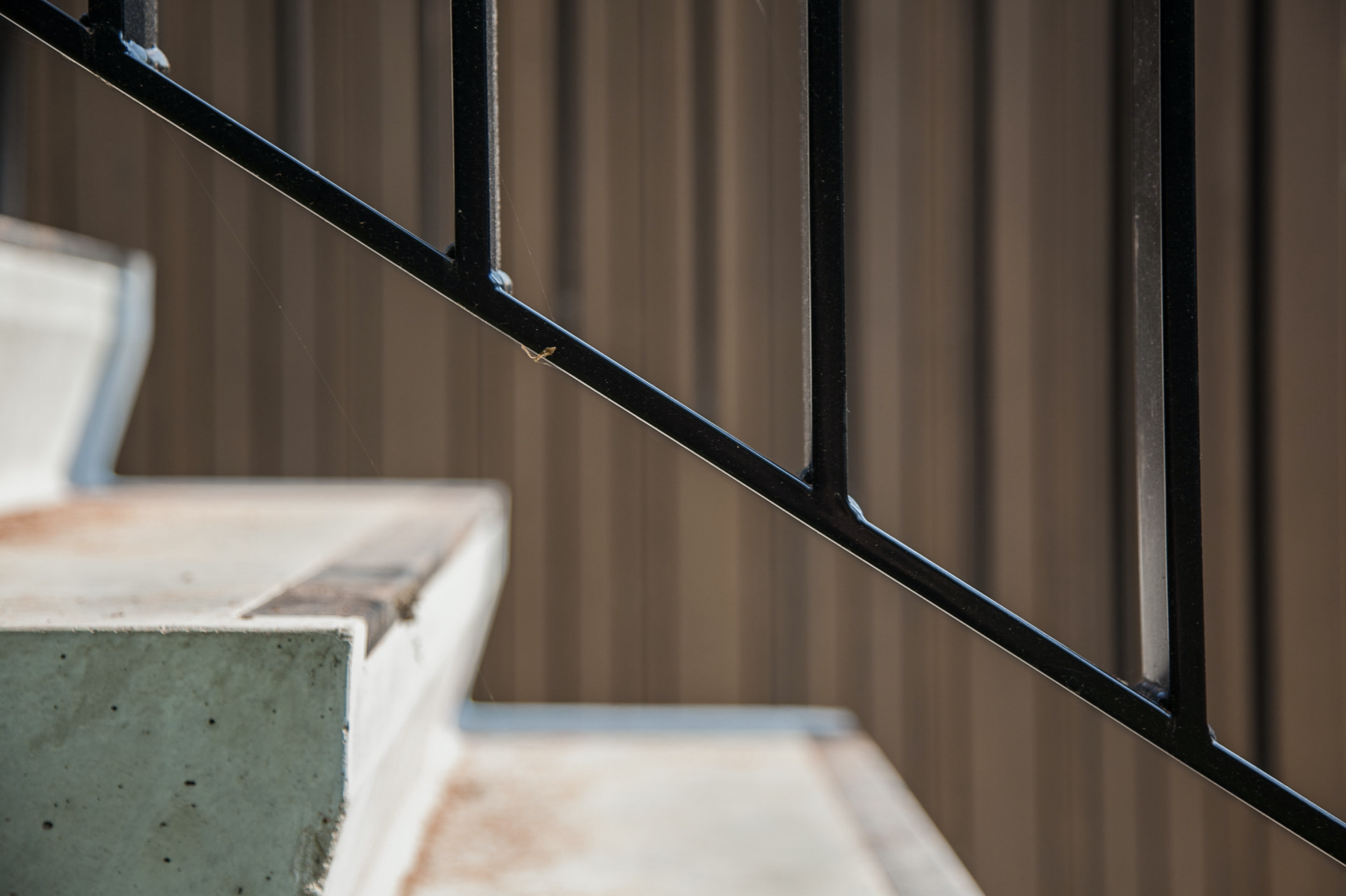 Architectural detail of a concrete staircase with a black metal handrail against wooden wall paneling, by Tom Naeyaert Architecture.