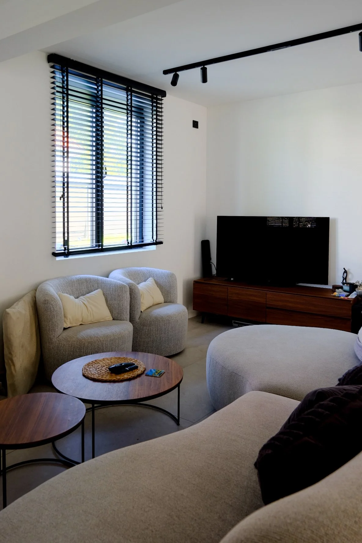 Contemporary residential living room project with a curved beige sofa, custom cabinetry, and modern track lighting, by Tom Naeyaert Architecture.