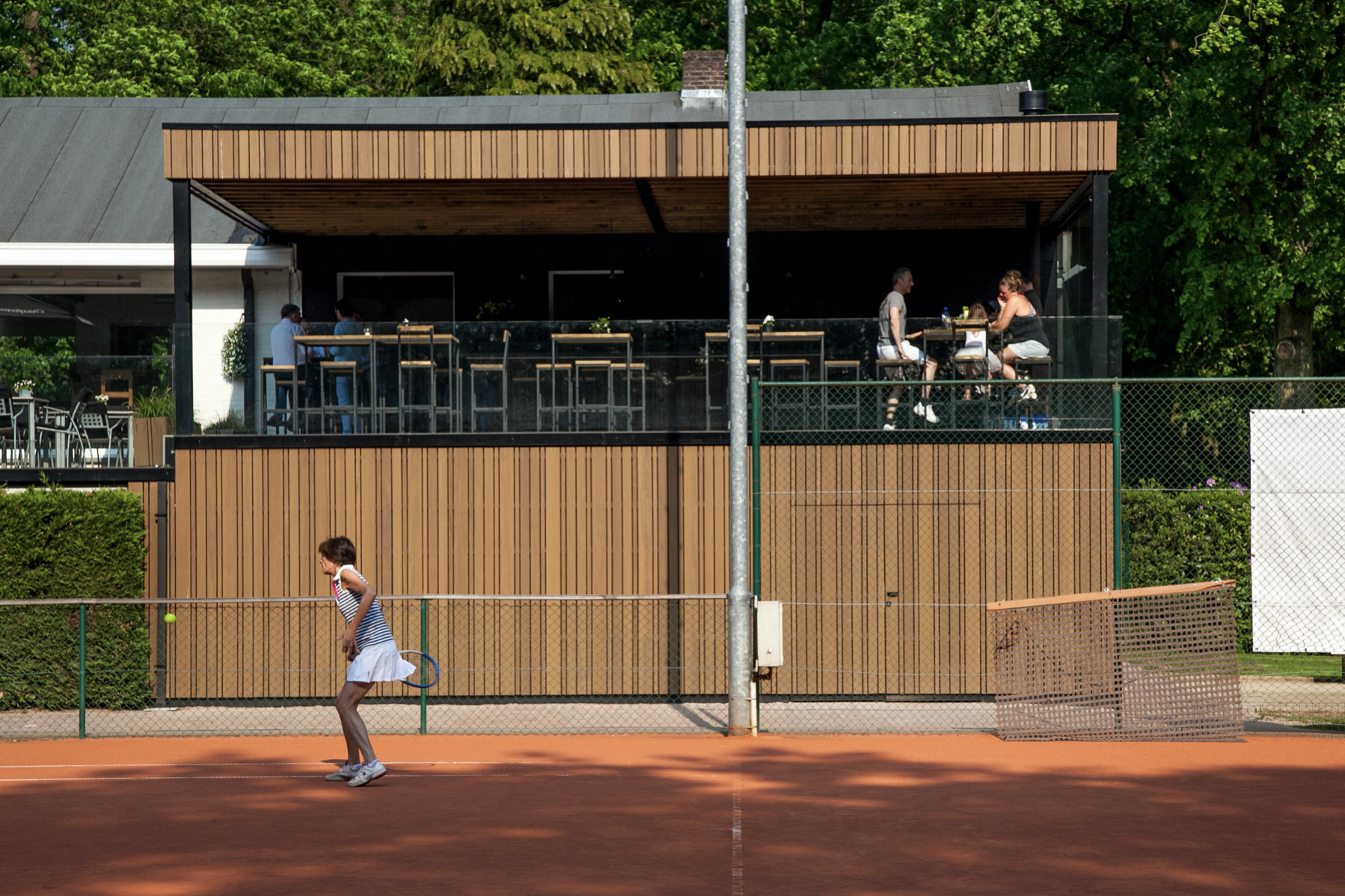 Contemporary clubhouse architecture with wooden cladding and a spacious balcony seating area, by Tom Naeyaert Architecture in Antwerp.