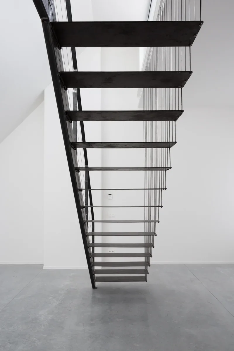 Modern staircase with black steps and metal railings against a white wall.