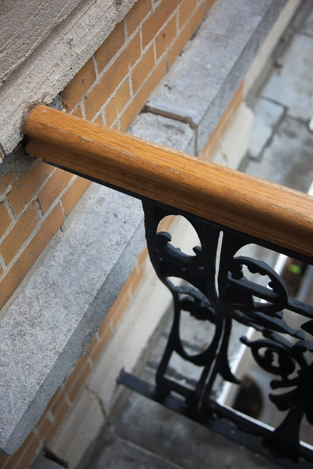 Close-up view of a wooden handrail attached to a brick and concrete wall on a balcony with an ornate black metal railing.