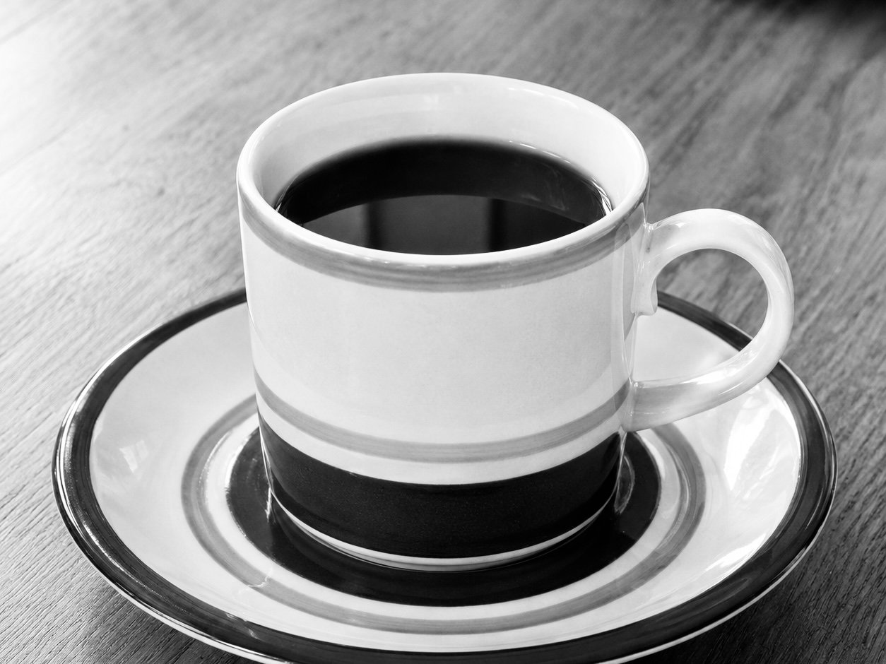 Mustavalkoinen kuva kahvikupista ja lautasesta pöydällä. Kirpputori Vanha Kotka kahvila. Café Vanha Kotka.