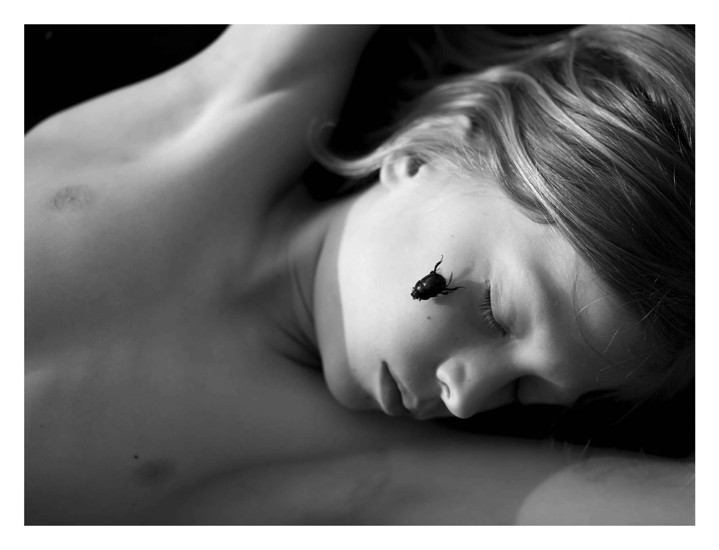 Black and white photograph of a woman with closed eyes, her head tilted to the side, and long hair. A ladybug is on her shoulder.