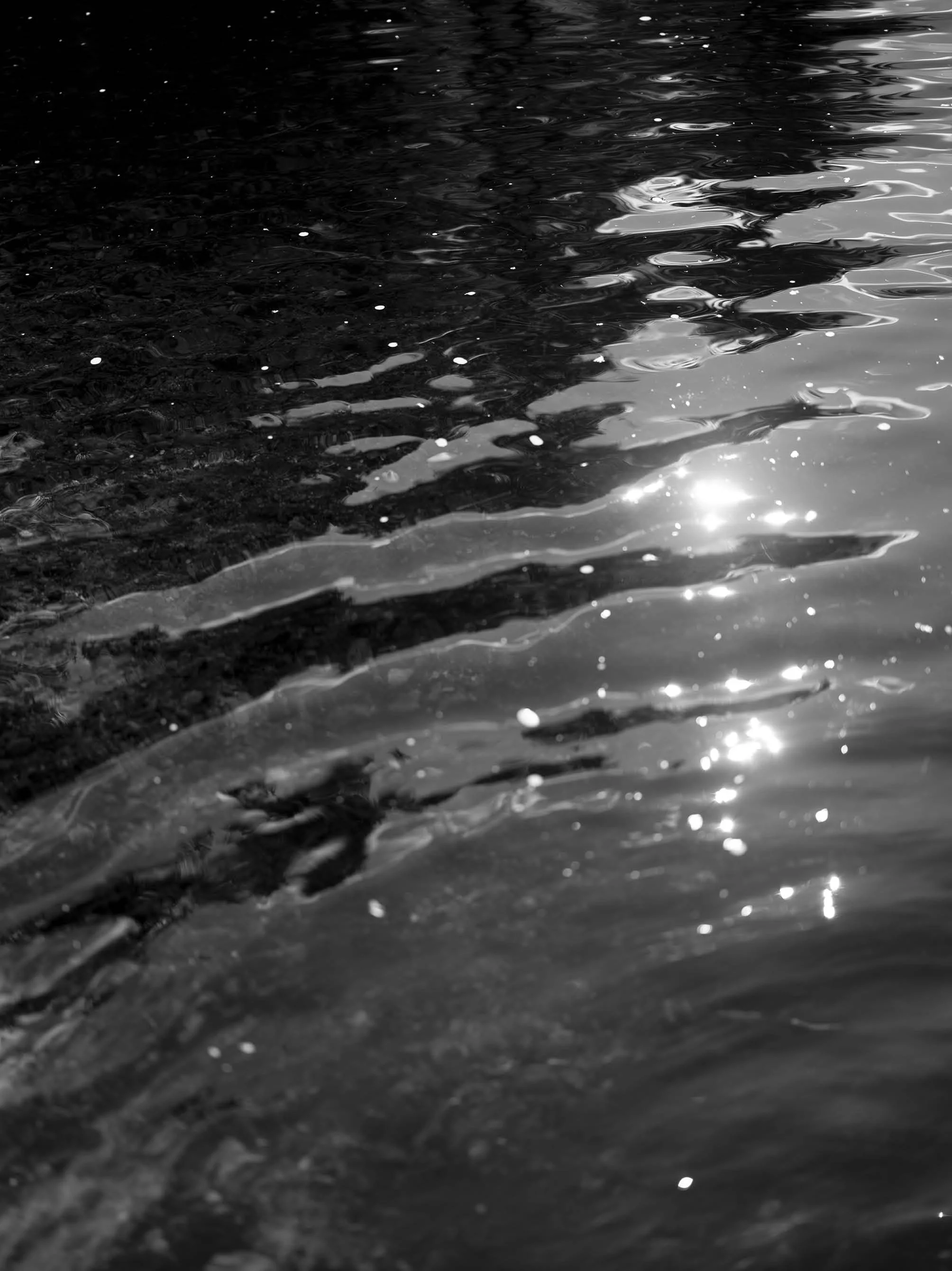 Close-up of rippling water on a dark surface with light reflecting off the surface.