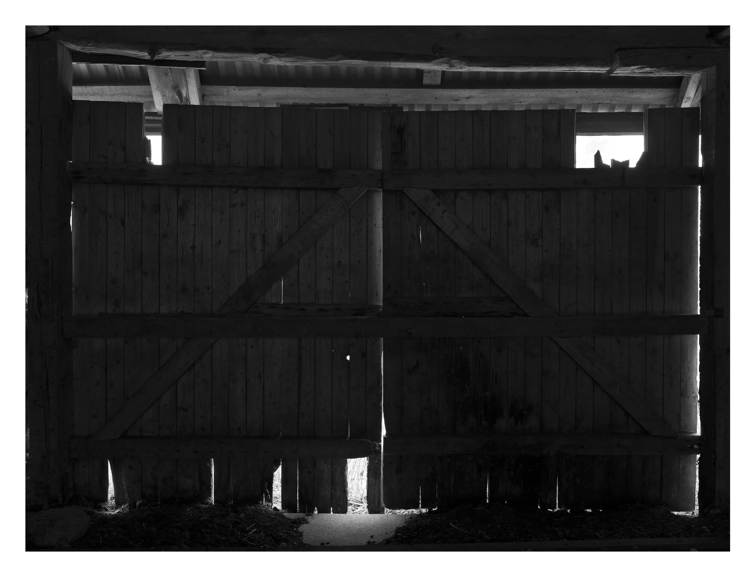Inside a barn, looking out through the open double doors, with sunlight shining through the gaps.