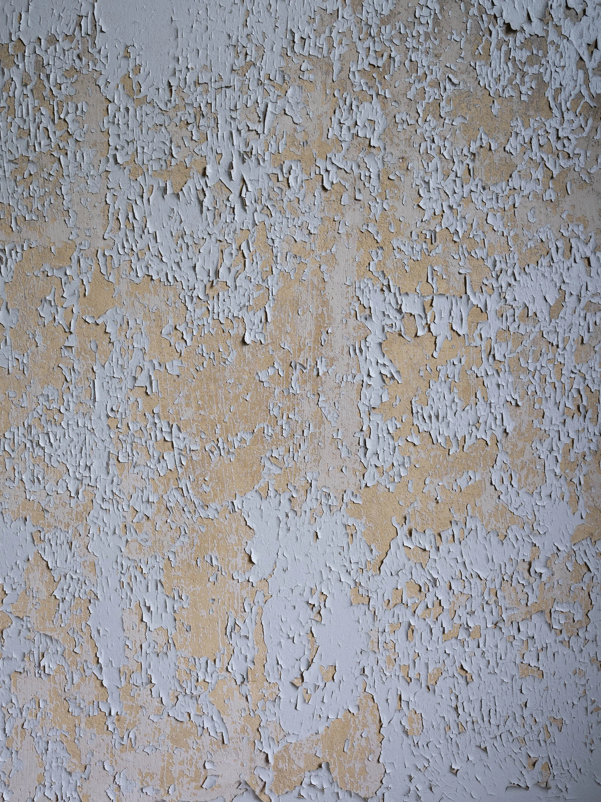 Close-up of weathered beige wall with light blue peeling paint.