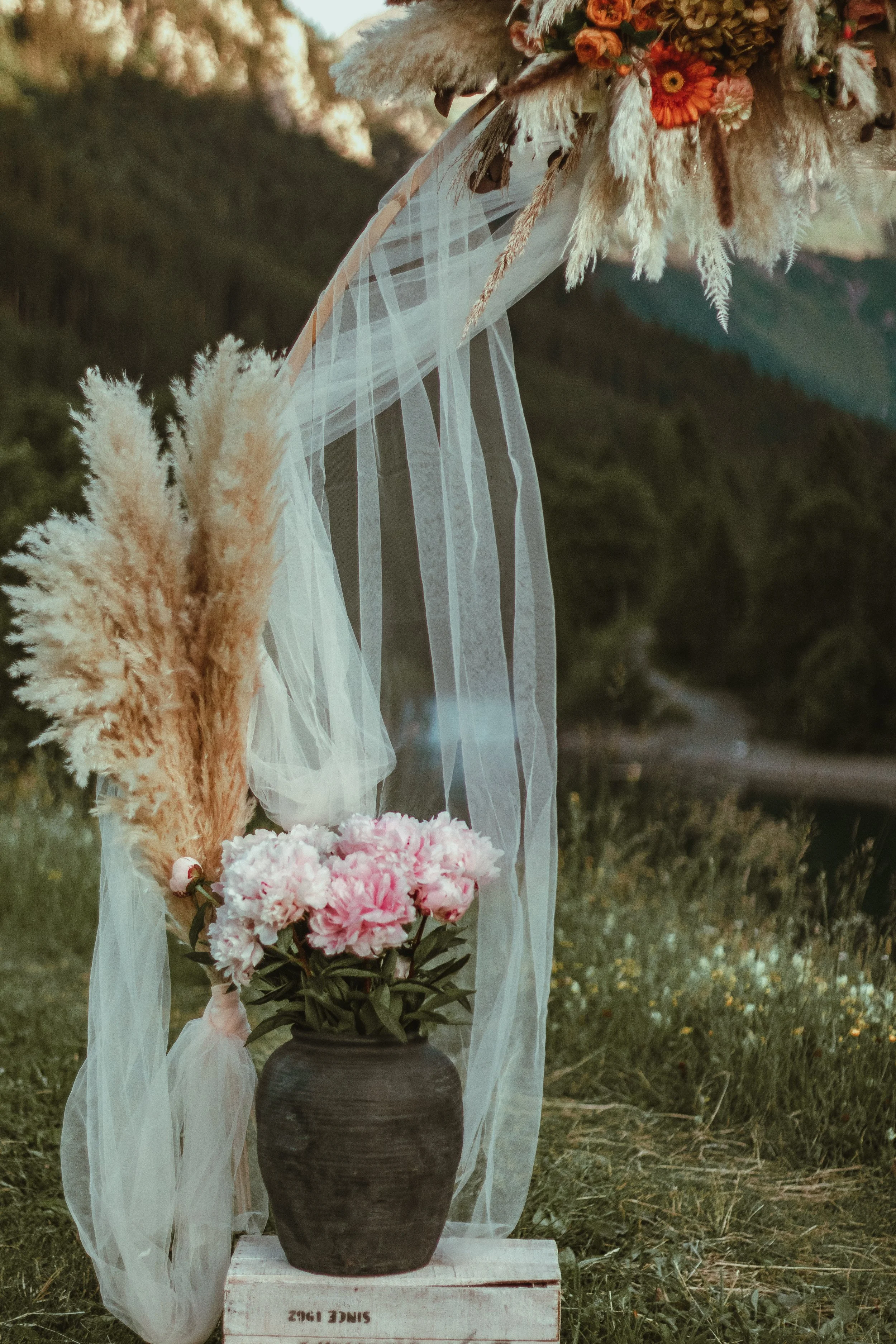 Decorative flower arrangement for an engagement photoshoot in a black pottery vase, with an arch with dried flowers and pampas grass, placed outdoors for a surprise proposal in Switzerland.