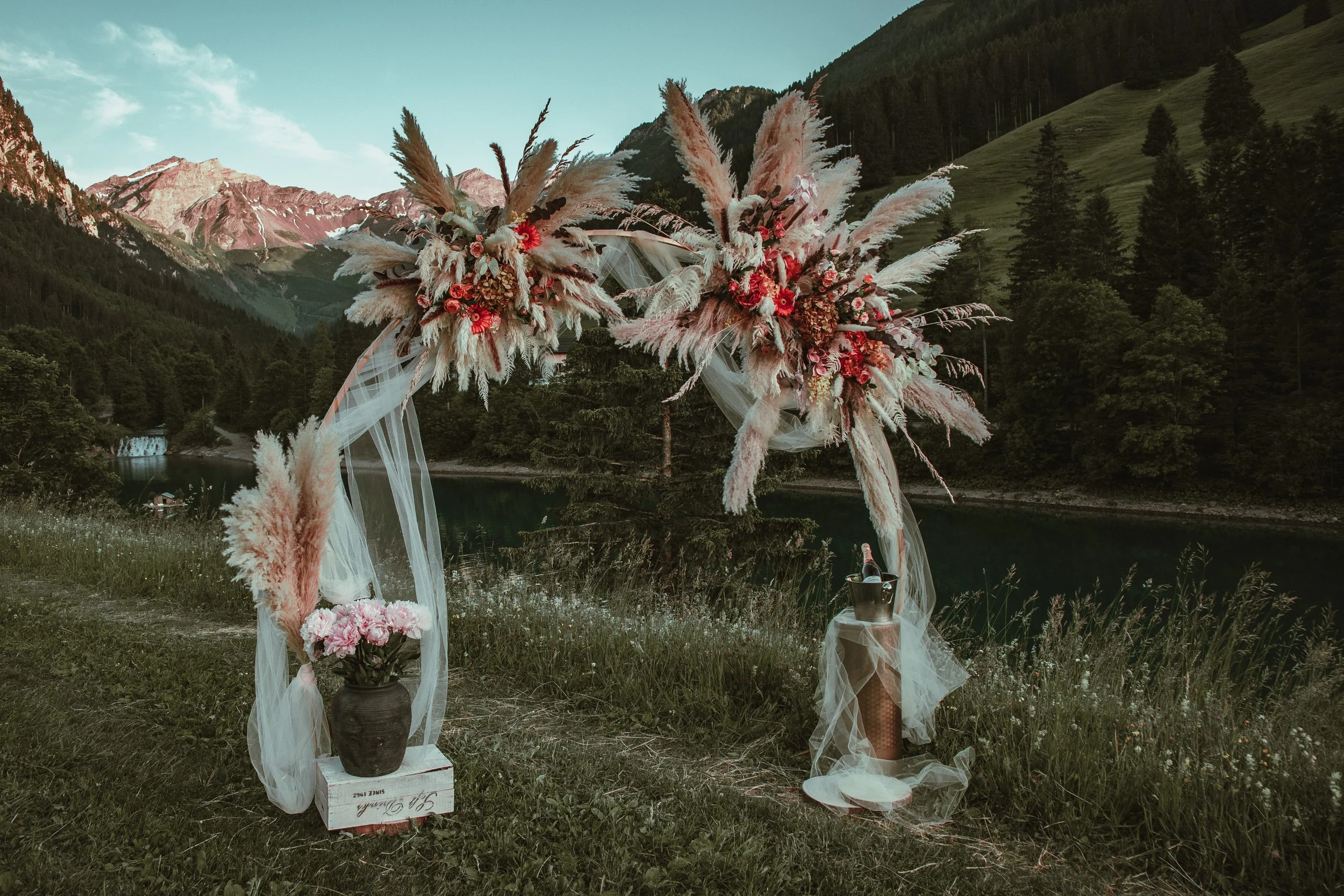 Romantic arch with dried florals, rustic style, a flower bouquet for a bride-to-be, Moët & Chandon champagne chilled in an ice bucket, romantic engagement photoshoot in a scenic Swiss outdoor setting.