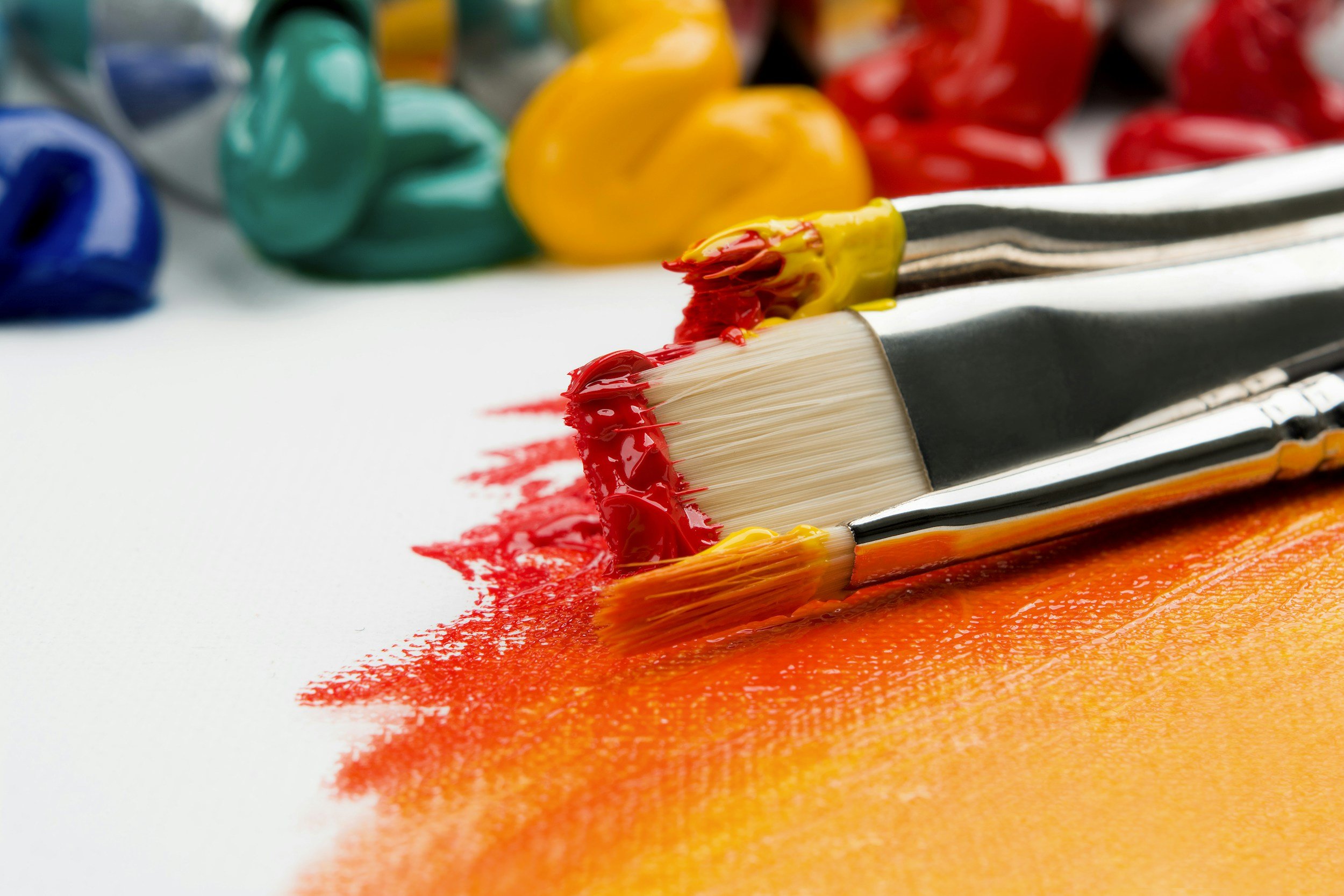 Paintbrushes with colorful paint on a white surface, surrounded by blobs of blue, green, yellow, and red paint.