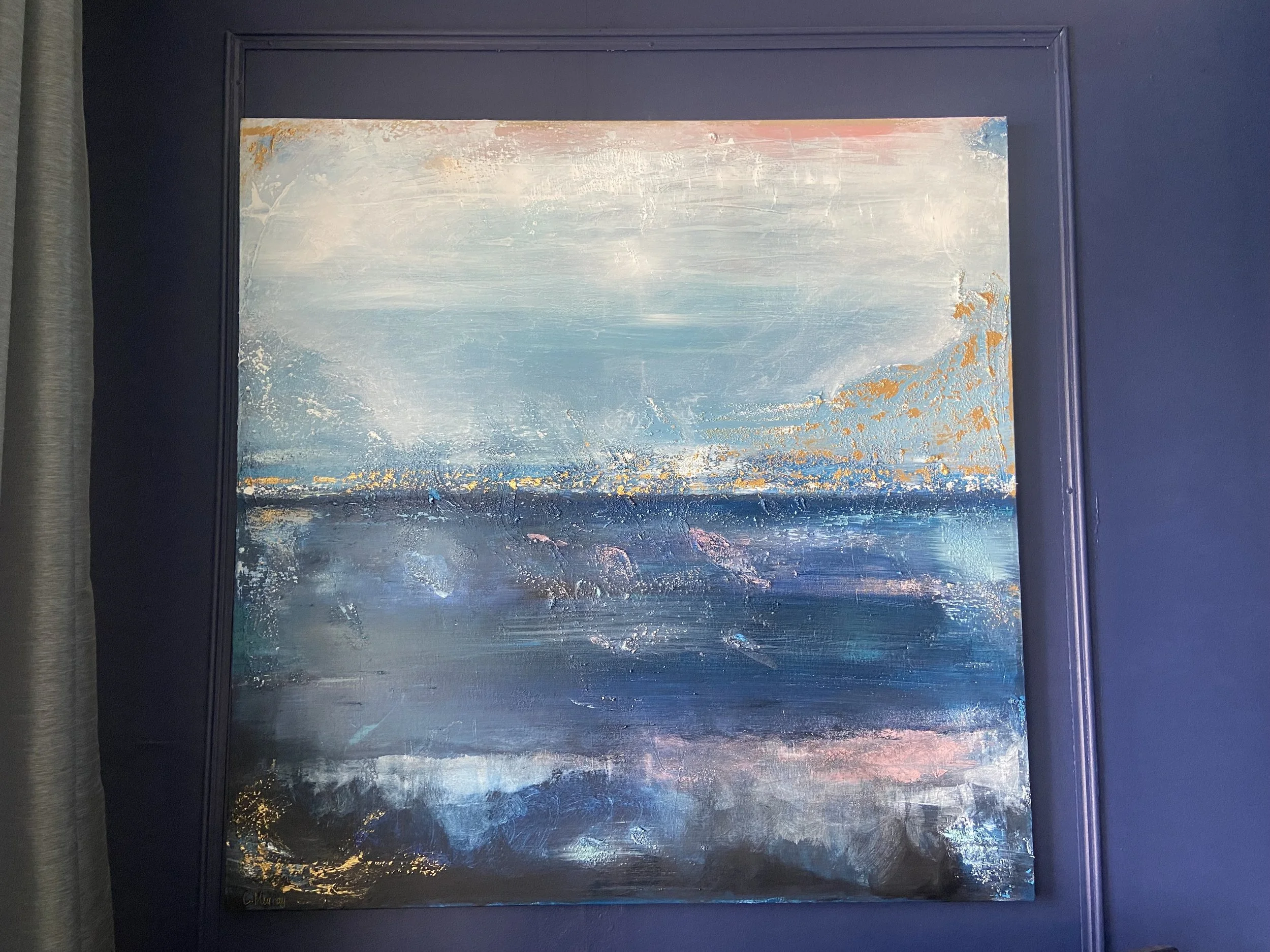 Abstract painting with shades of blue, white, and hints of gold, framed in black, hanging on a dark wall.