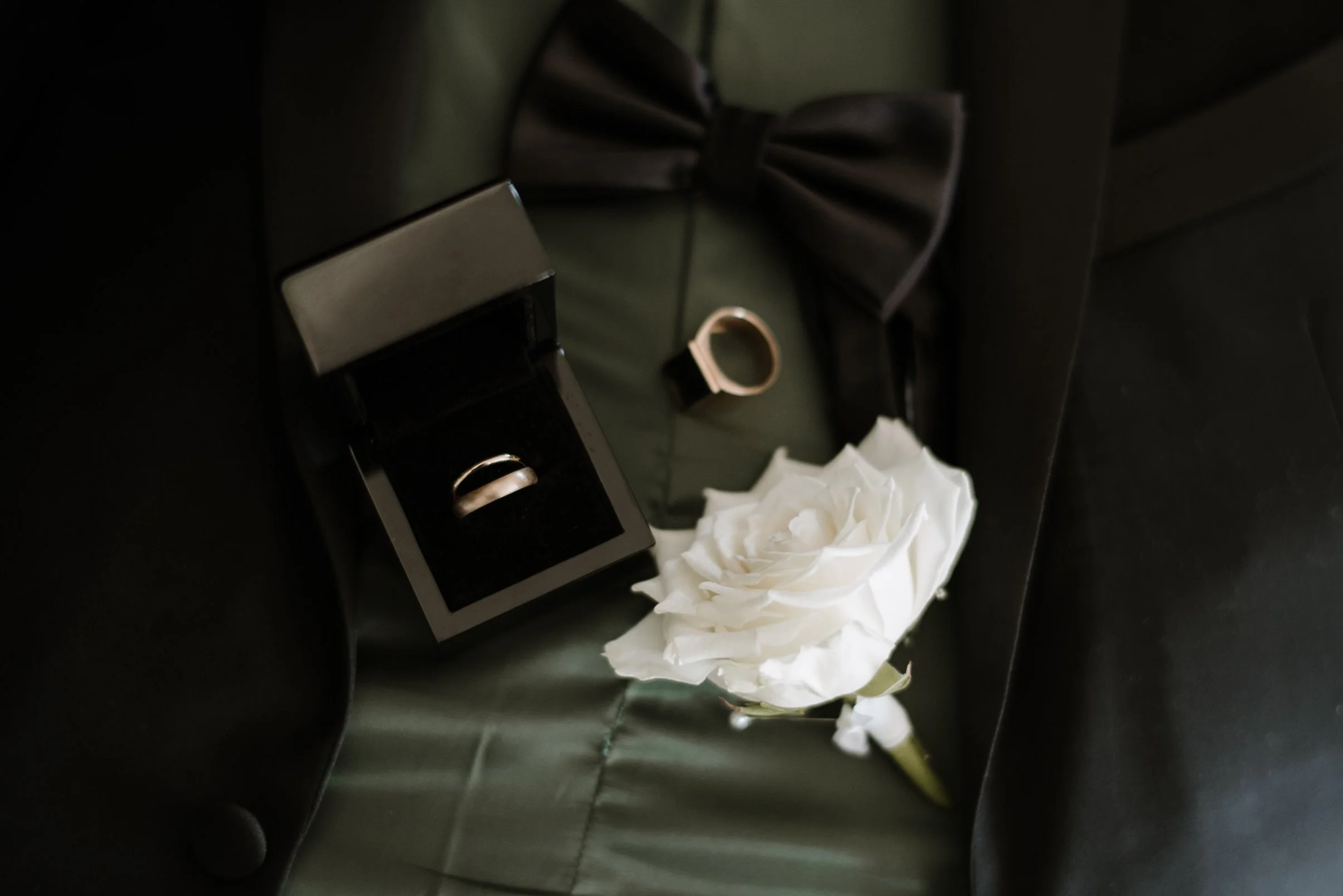 A crumpled white flower lies on the floor next to a black and silver alarm clock, with a reflective black surface and a greenish background.