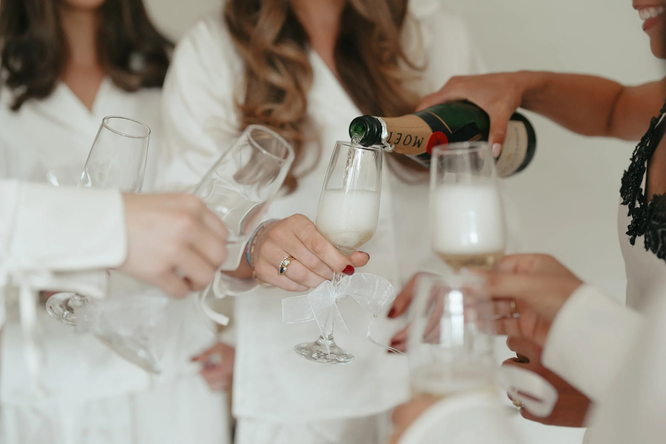 People in white attire celebrating, as one person pours champagne into a flute at a gathering or party.