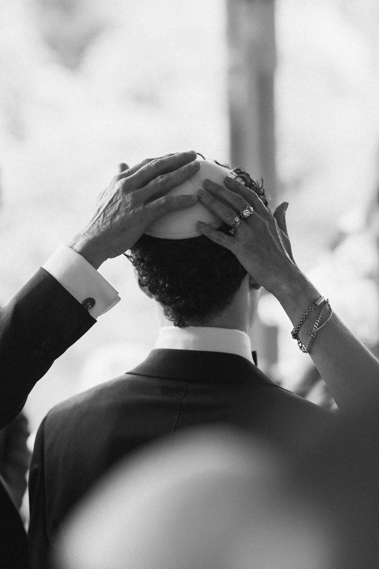 A person in a suit placing a circular object on their head, shown from the back in black and white.