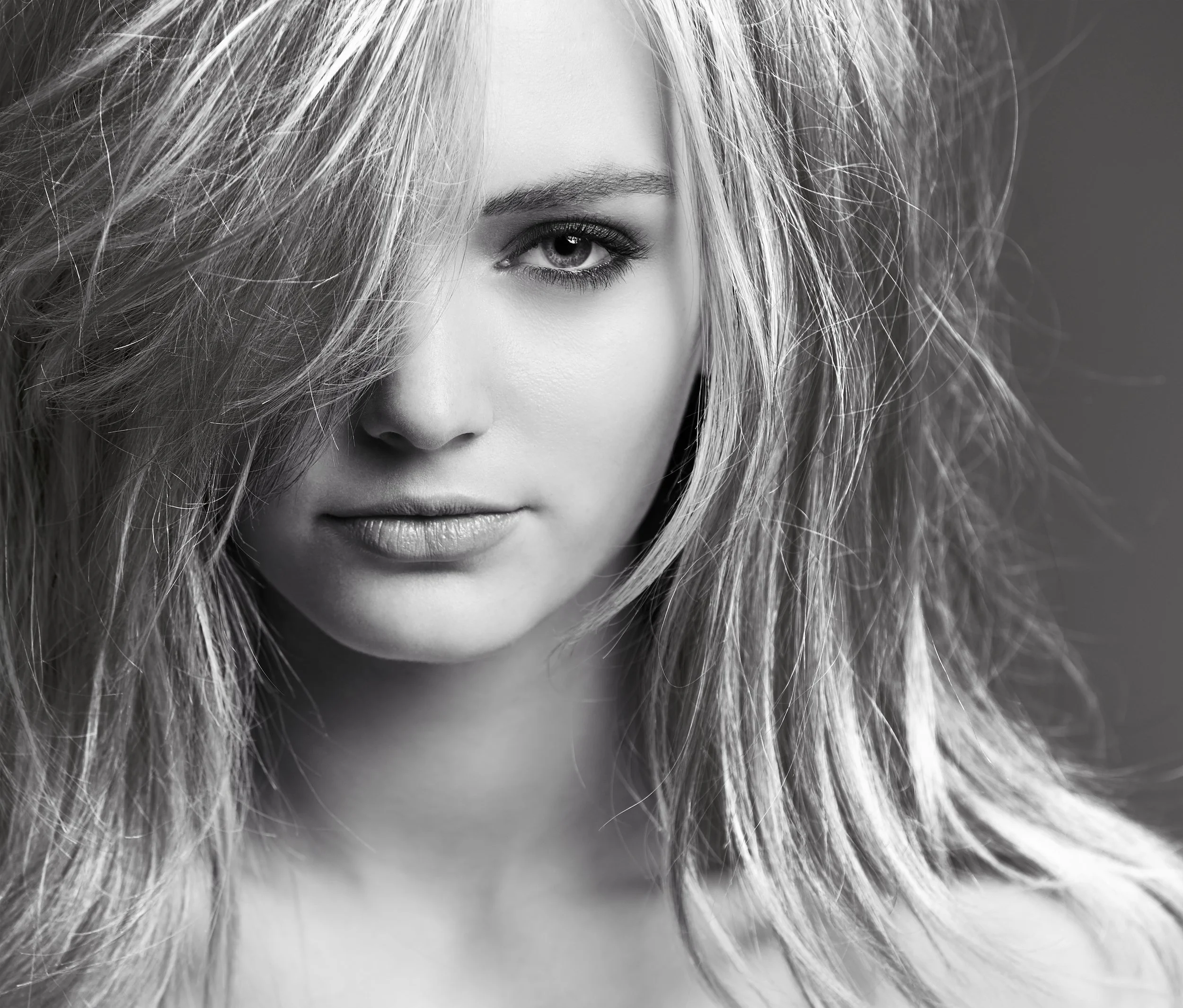 A black and white close-up of a woman's face, focusing on her eye, with voluminous, slightly messy hair surrounding her face.