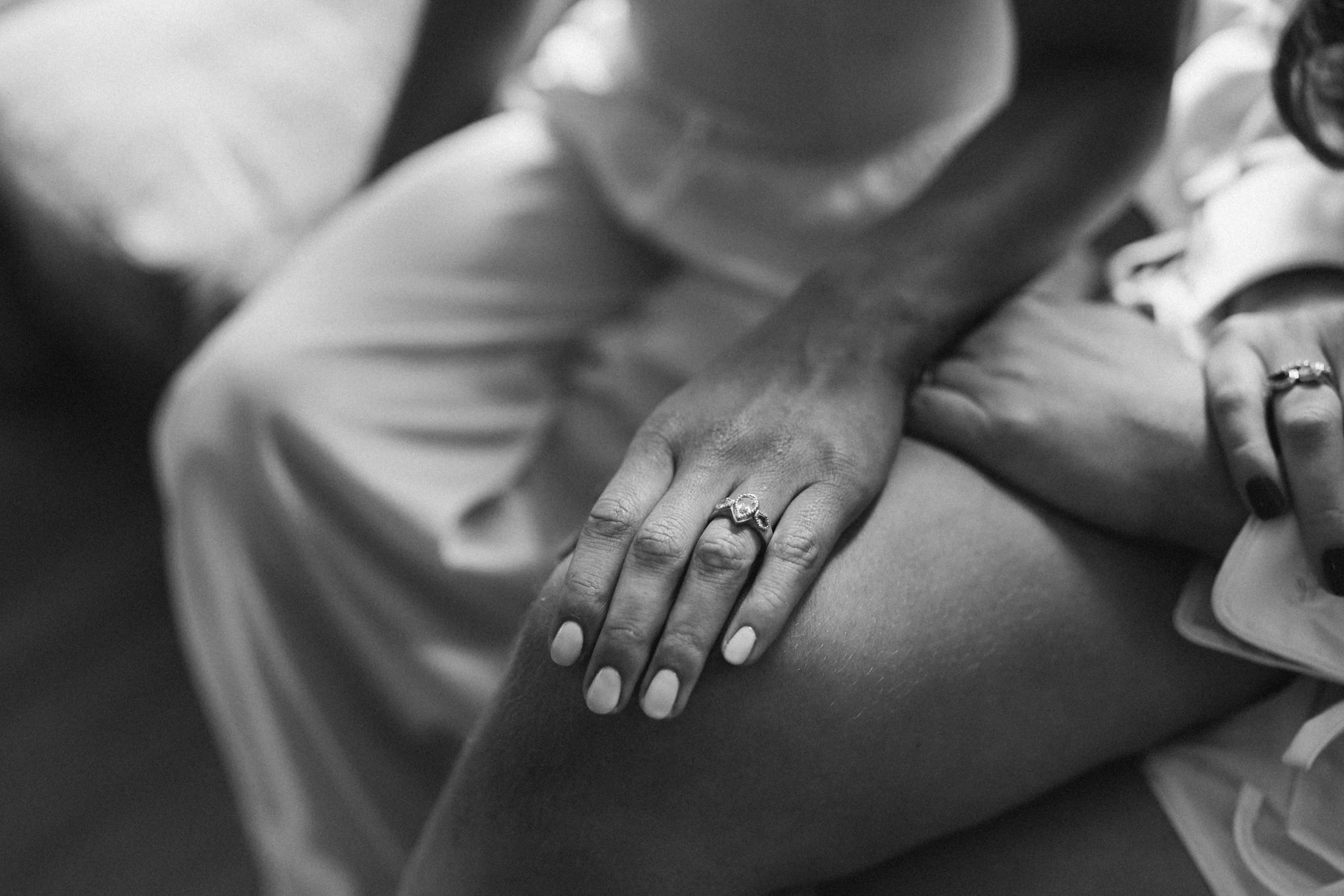 Close-up of two hands clasped together, with one hand resting on top of the other, wearing rings. The image is in black and white.