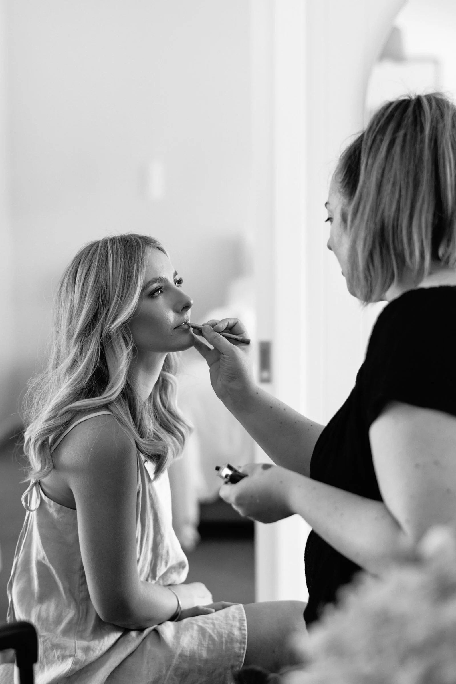 A woman sitting on a chair getting her makeup done by a makeup artist.