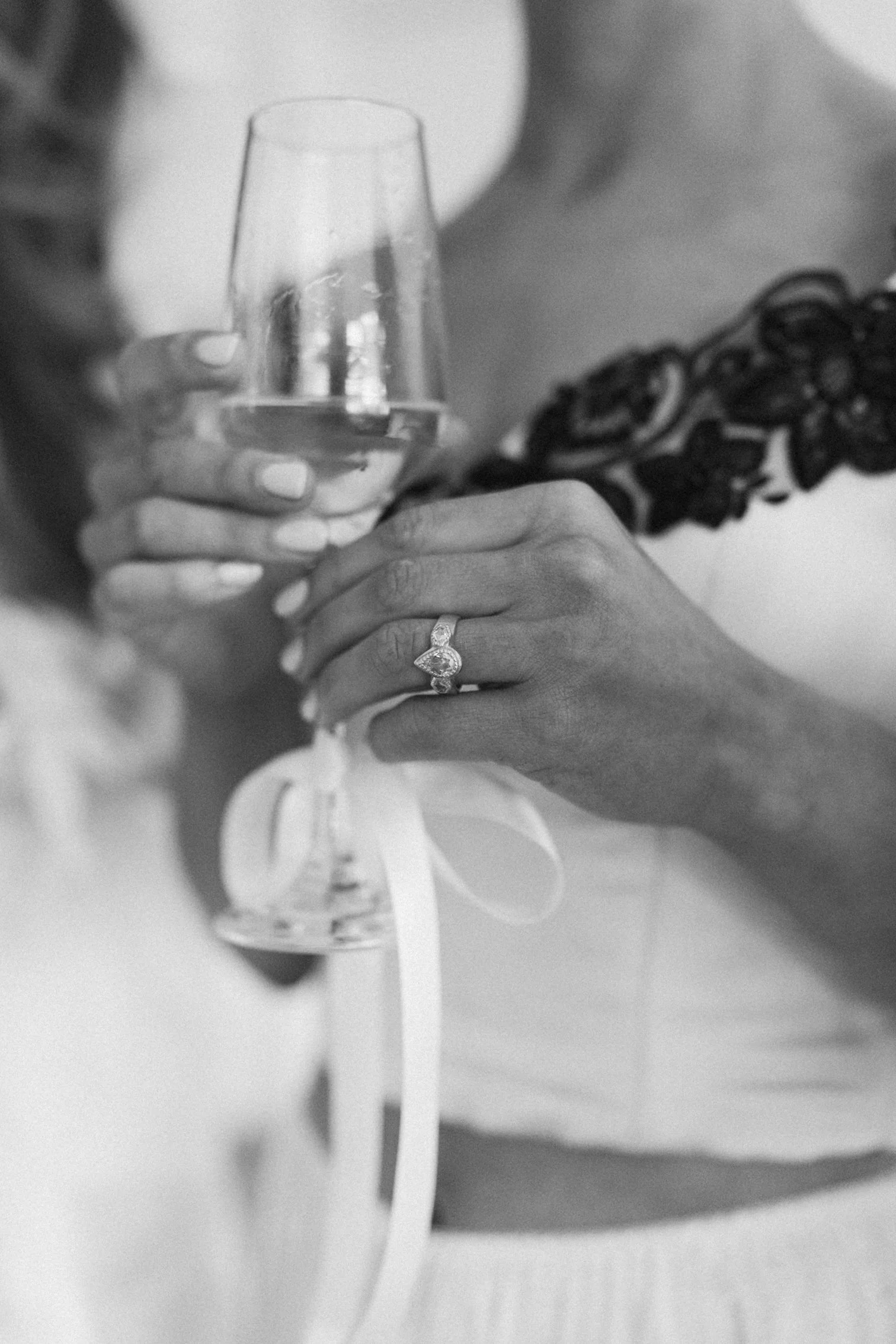 A person holding a glass of champagne, with a close-up of their hand and ring, in black and white.