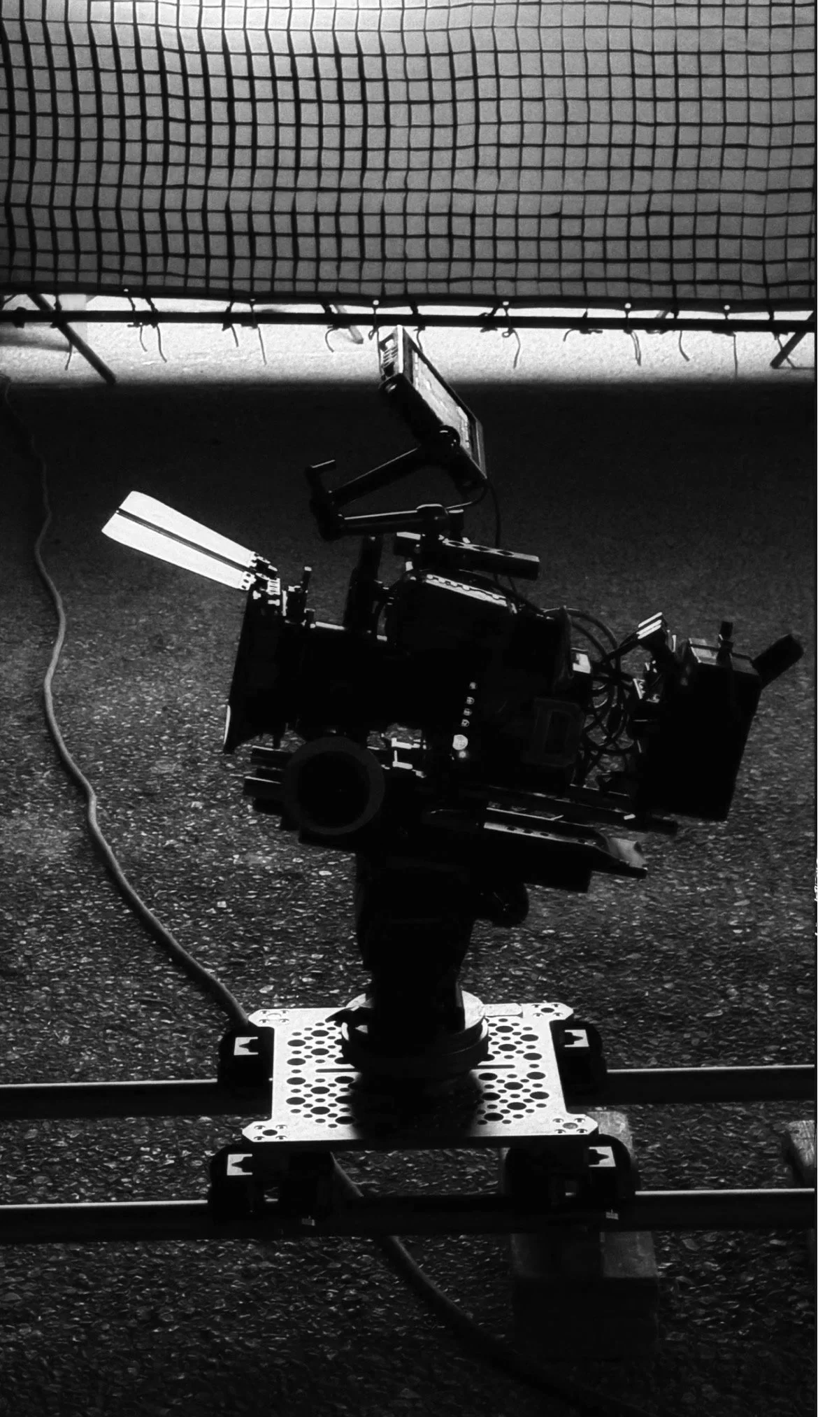 Een professionele filmcamera staat op een dolly op een ruige grond, gericht op een bedekking met een grid patroon.