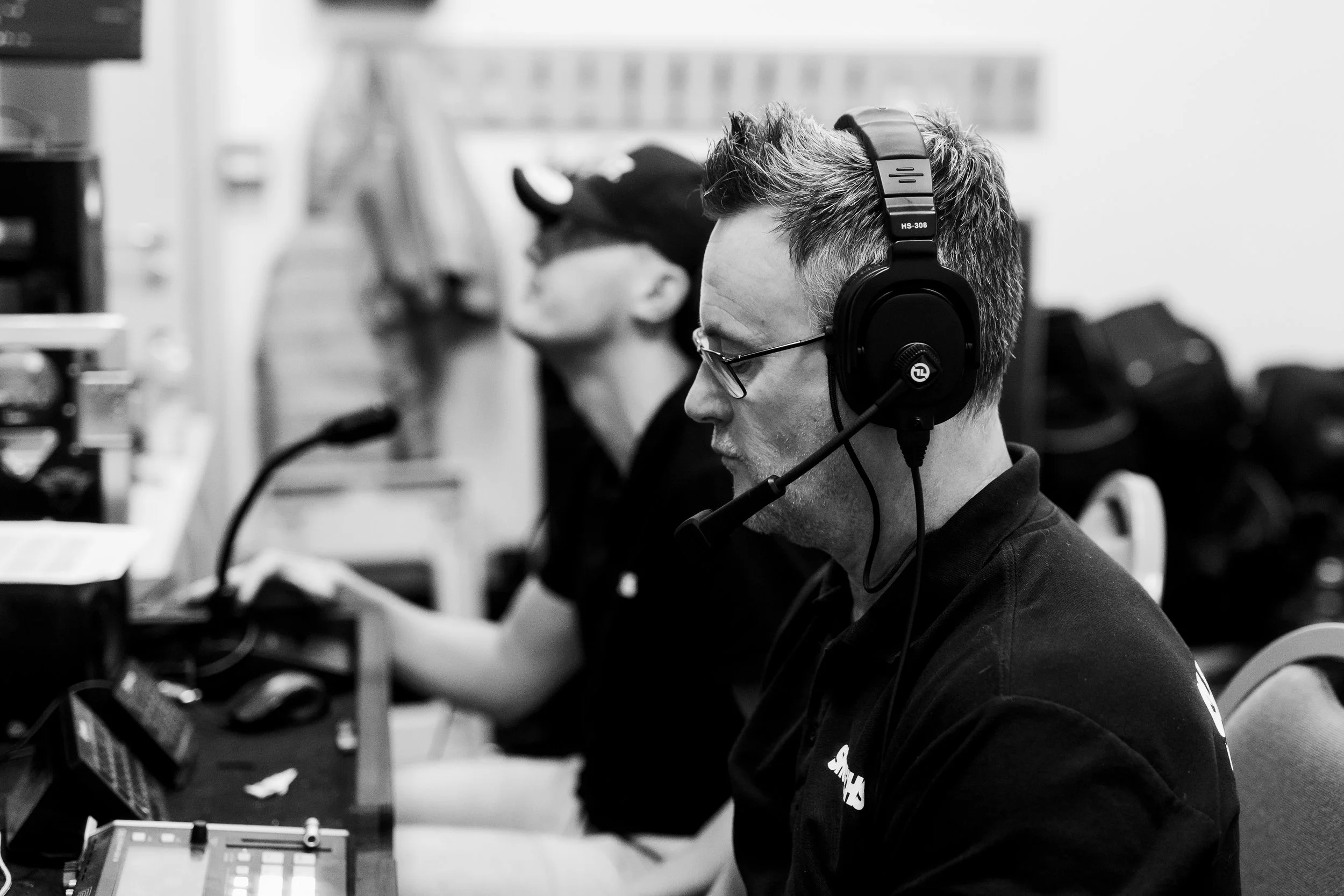 A man with glasses wearing a headset and working on electronic equipment in a workshop or studio.