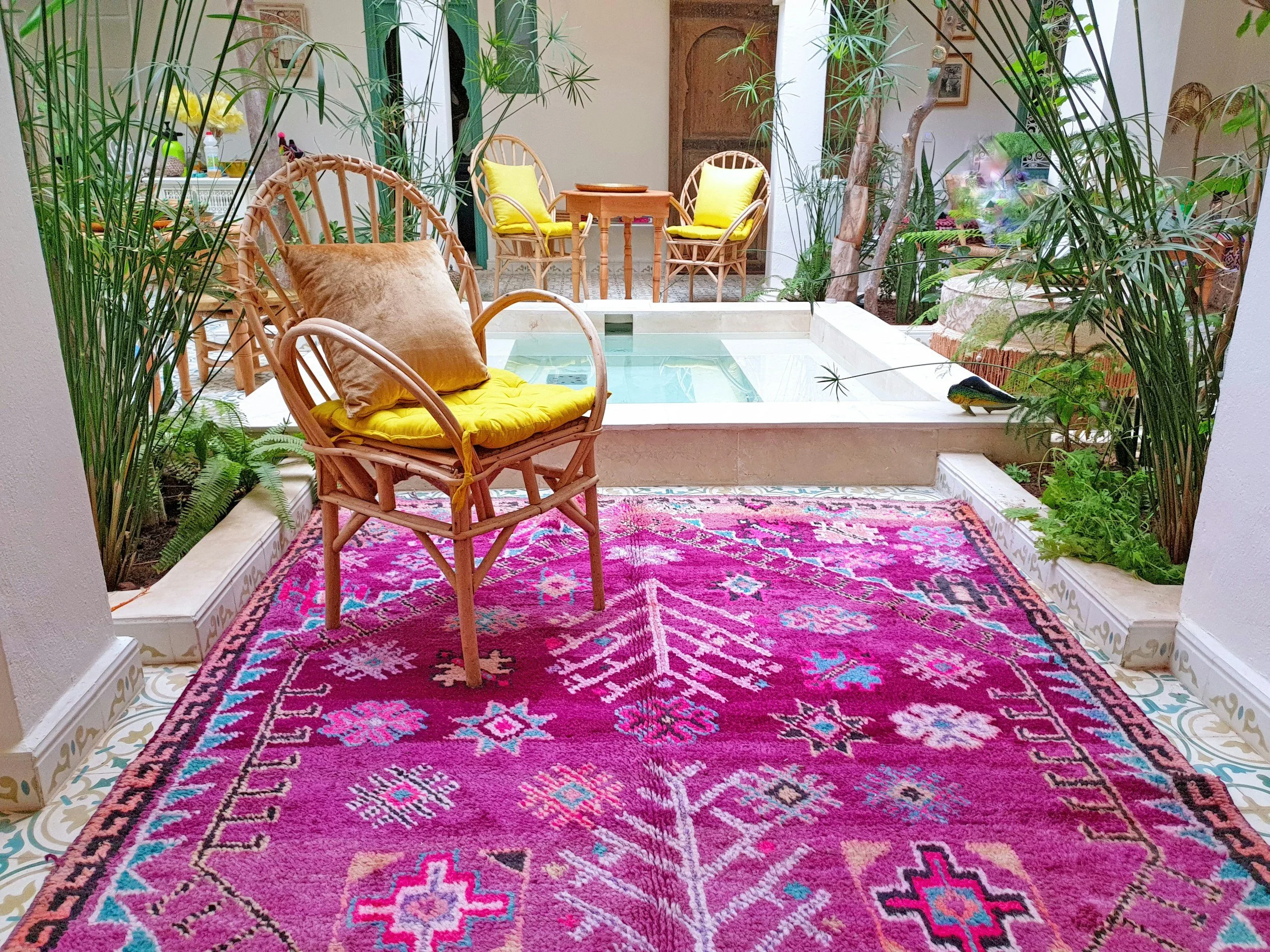 Bespoke Moroccan event styling featuring a bright pink vintage rug, natural rattan lounge chairs with yellow cushions, and an intimate courtyard pool setup.