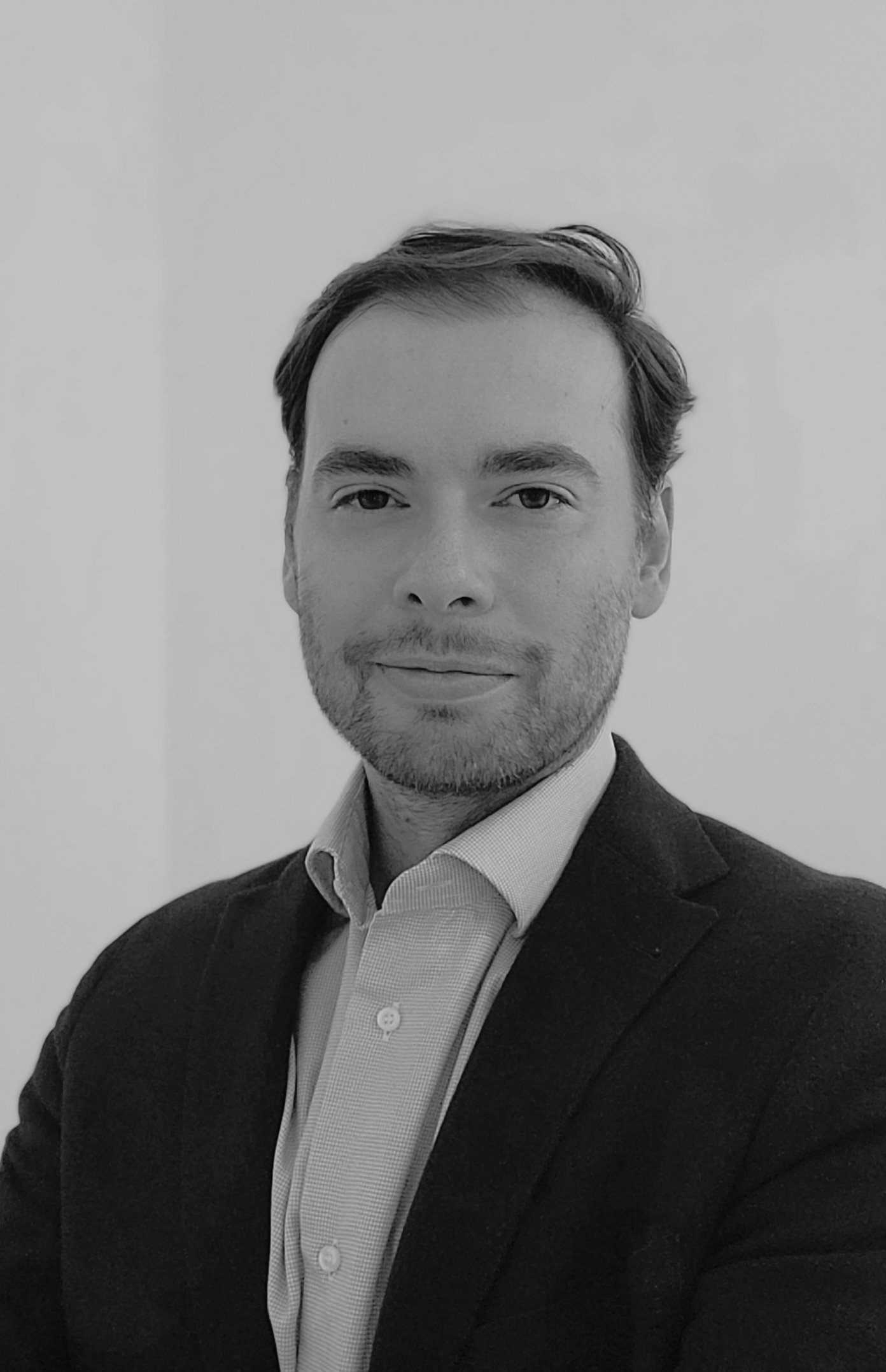 A black and white photo of a man in a suit and collared shirt, with neatly styled hair and light facial hair, against a plain background.