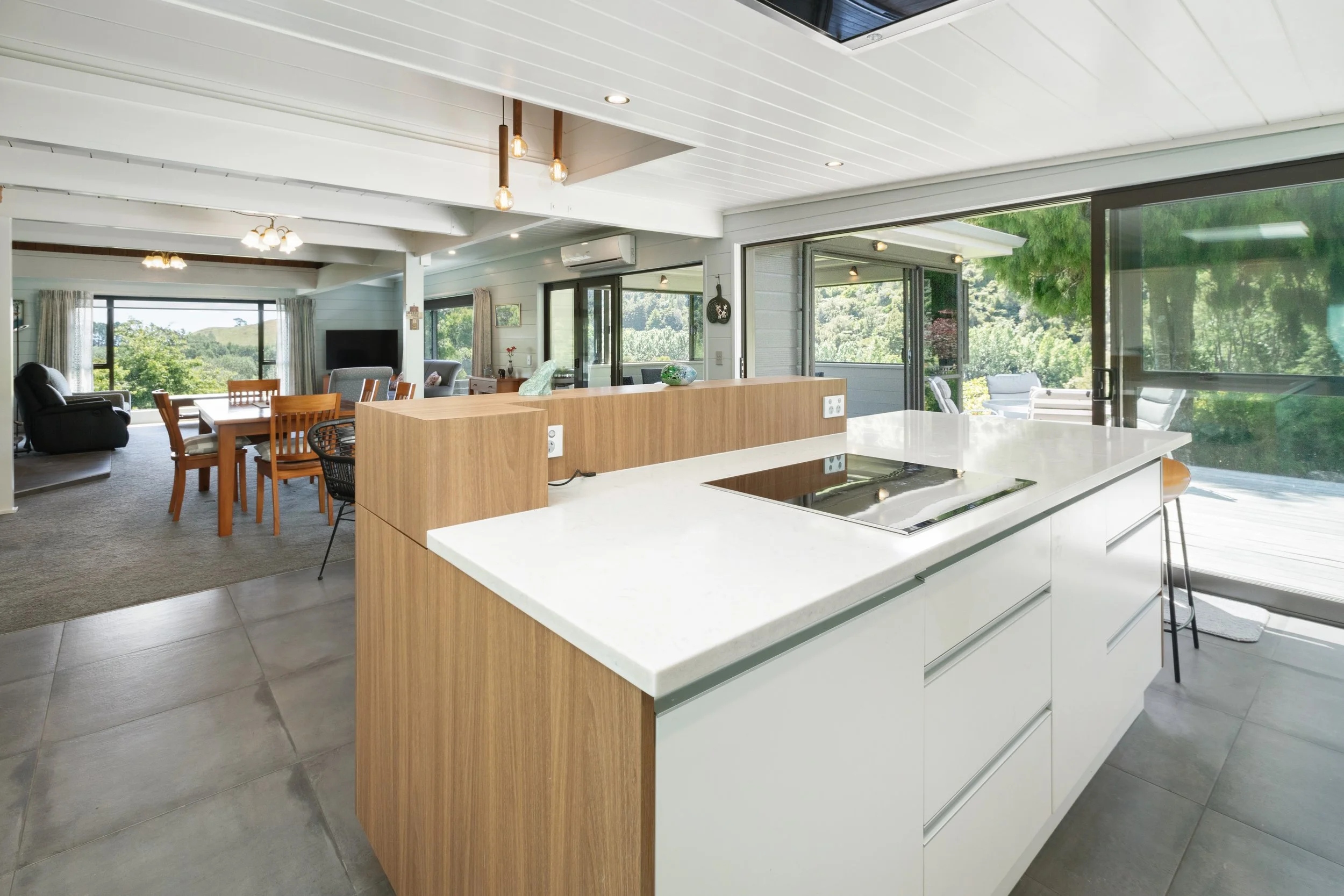 Kitchen island with integrated cooktop and white quartz benchtop opening to living and outdoor deck, Maratoto Waikato