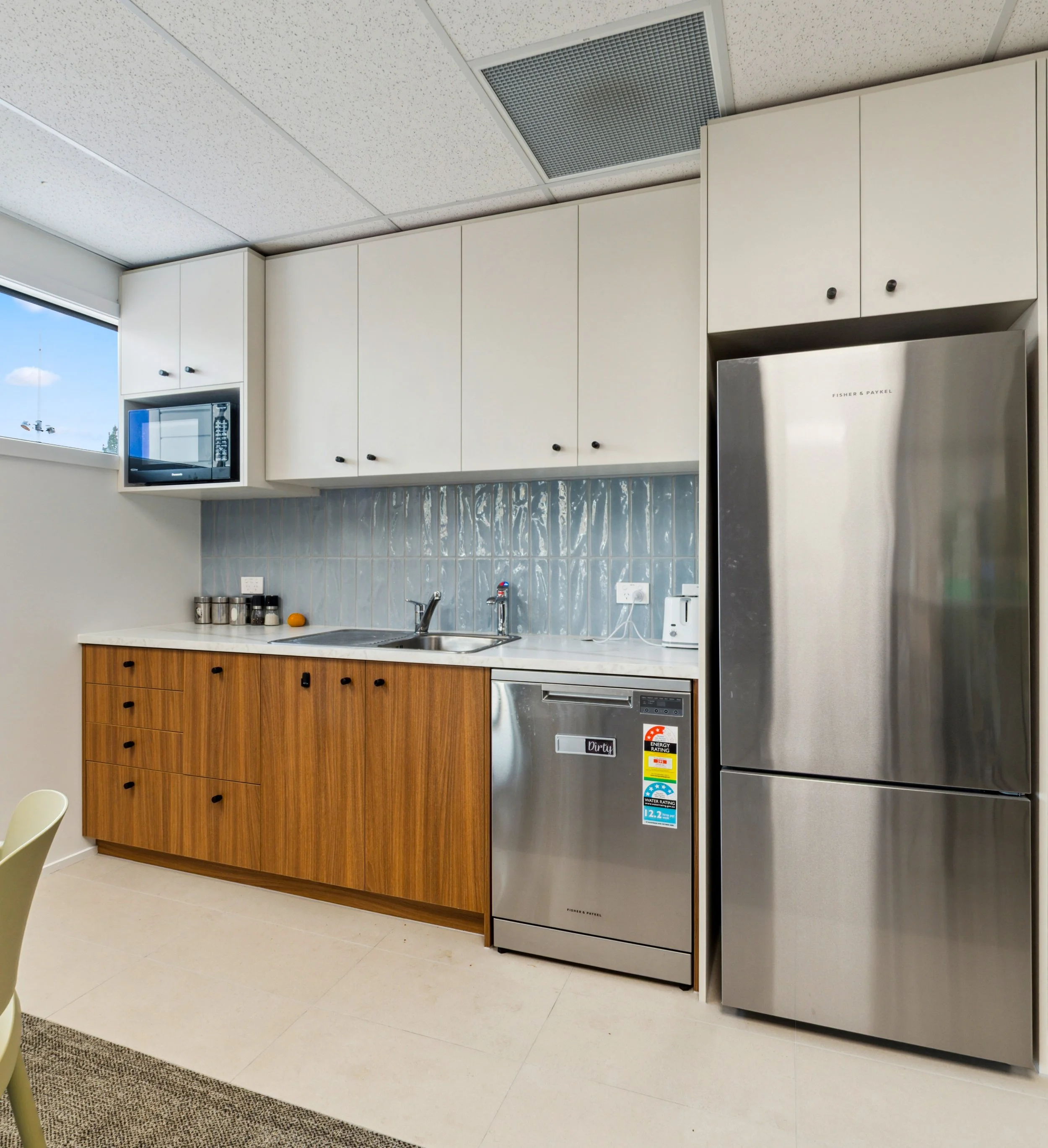 Staff kitchen with timber lower cabinetry, textured blue splashback and white uppers, Pukekohe commercial fitout