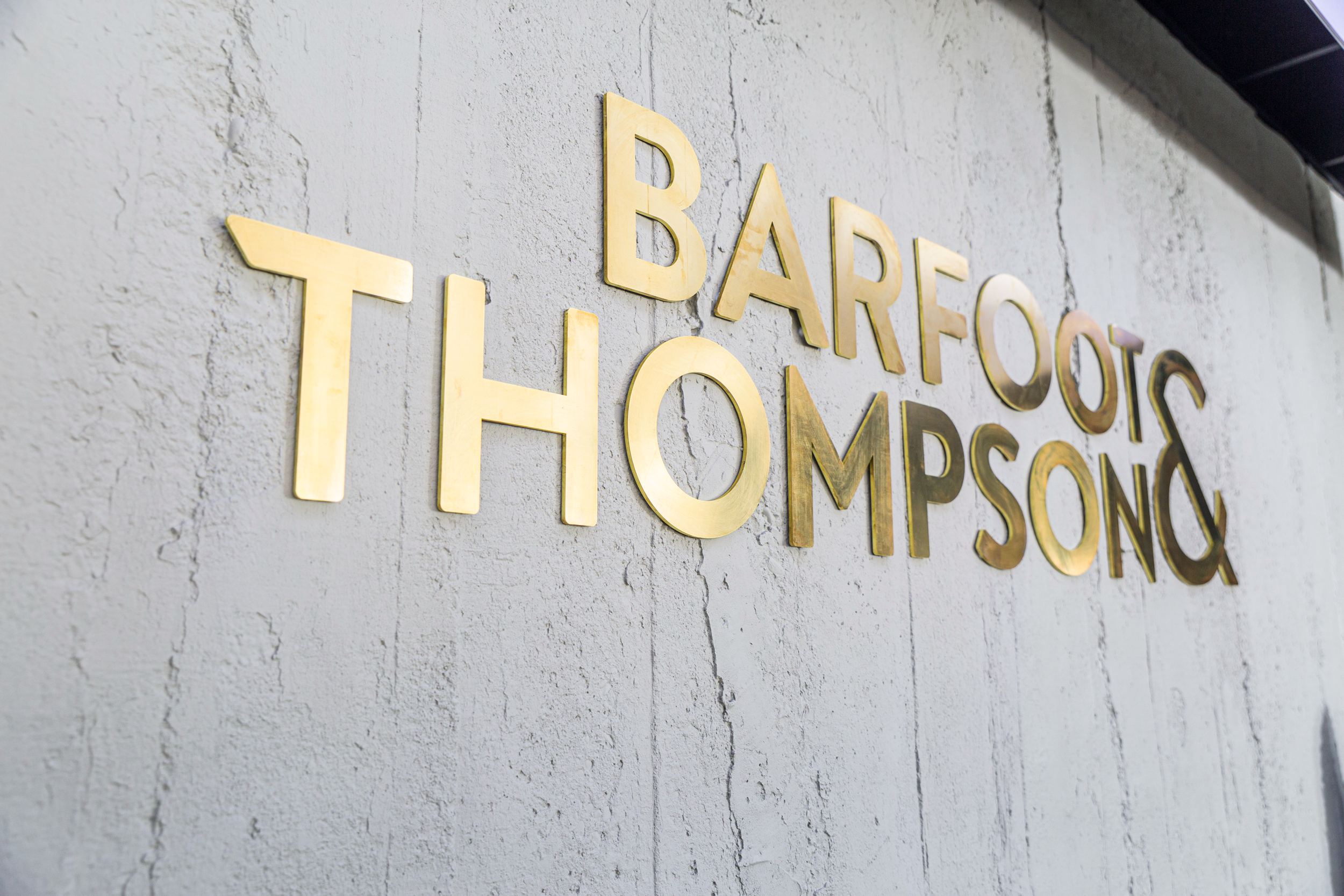 Barfoot Thompson Otahuhu gold signage on textured concrete interior wall, Auckland commercial fitout