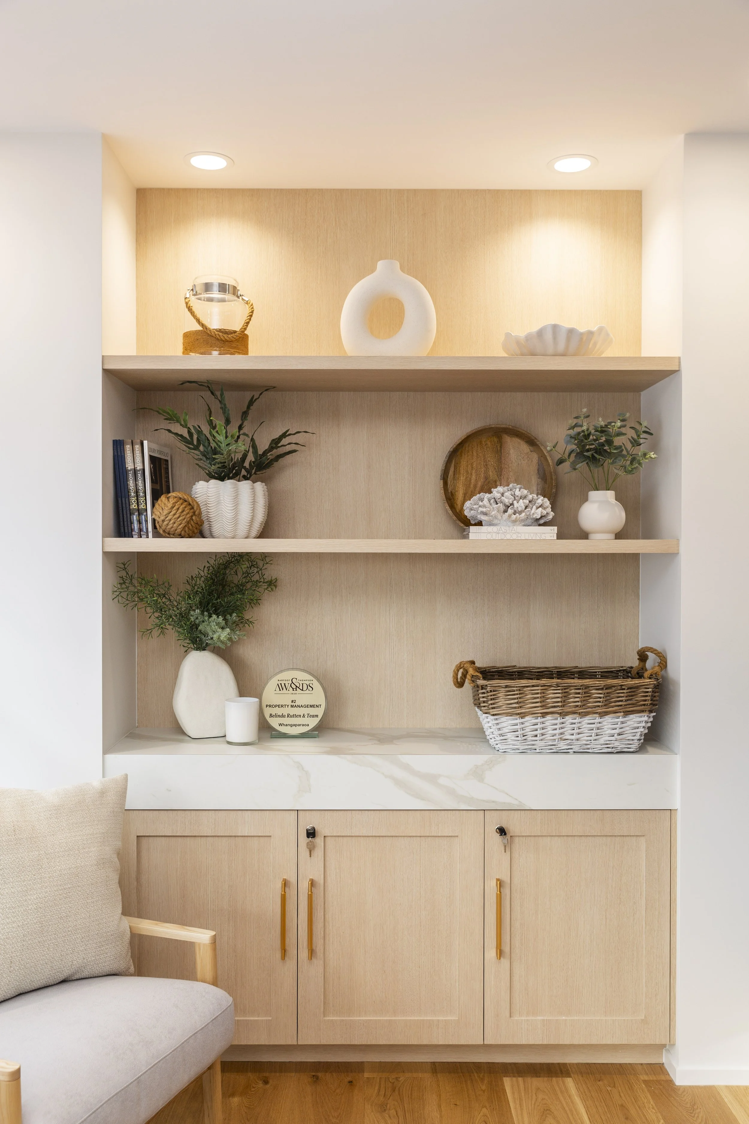 Styled built-in shelving with gold handles and coastal accessories, Barfoot Thompson Whangaparaoa office interior