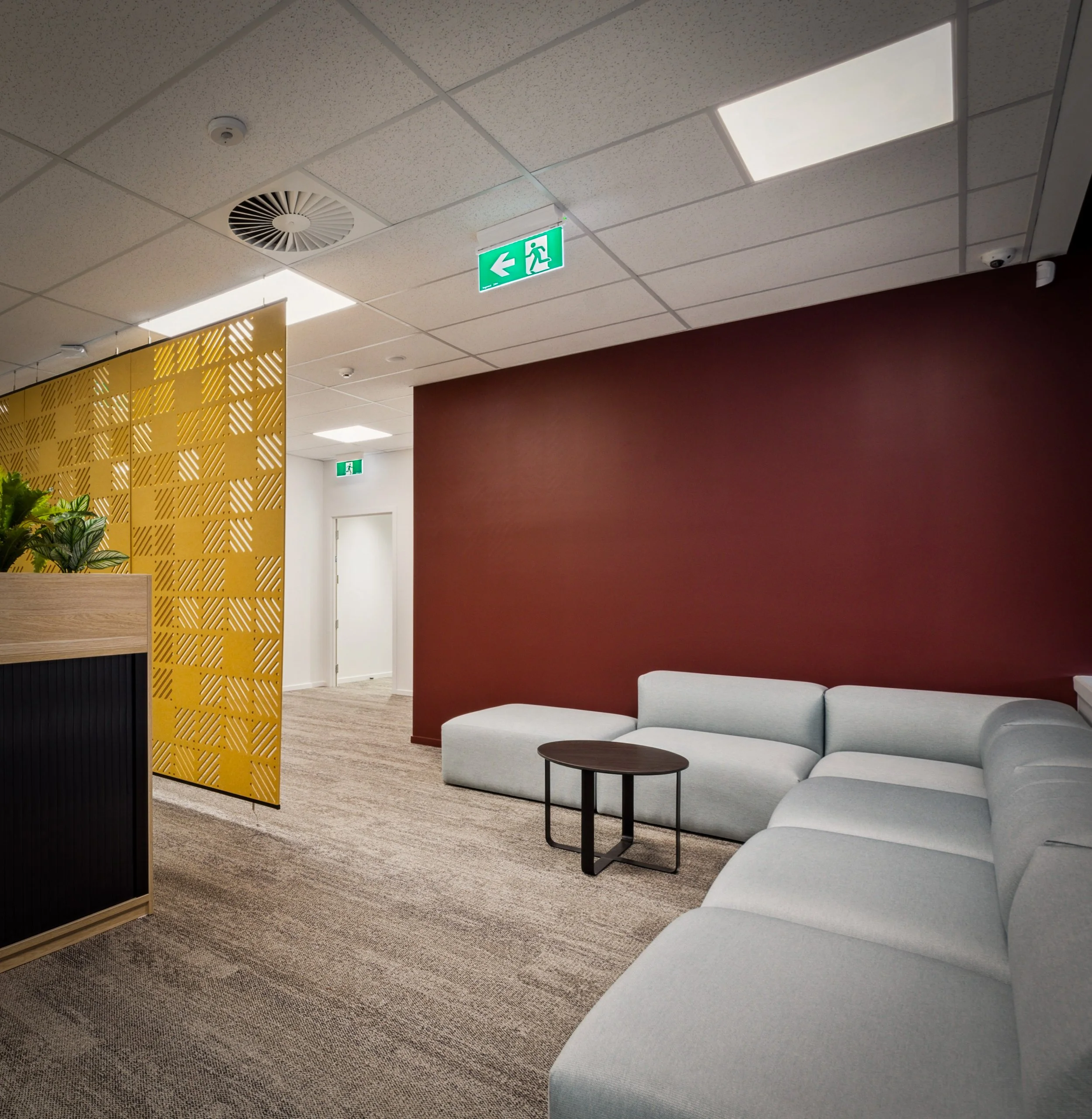 Office chill zone with modular sofa, burgundy wall and gold perforated screen, Barfoot Thompson Pukekohe