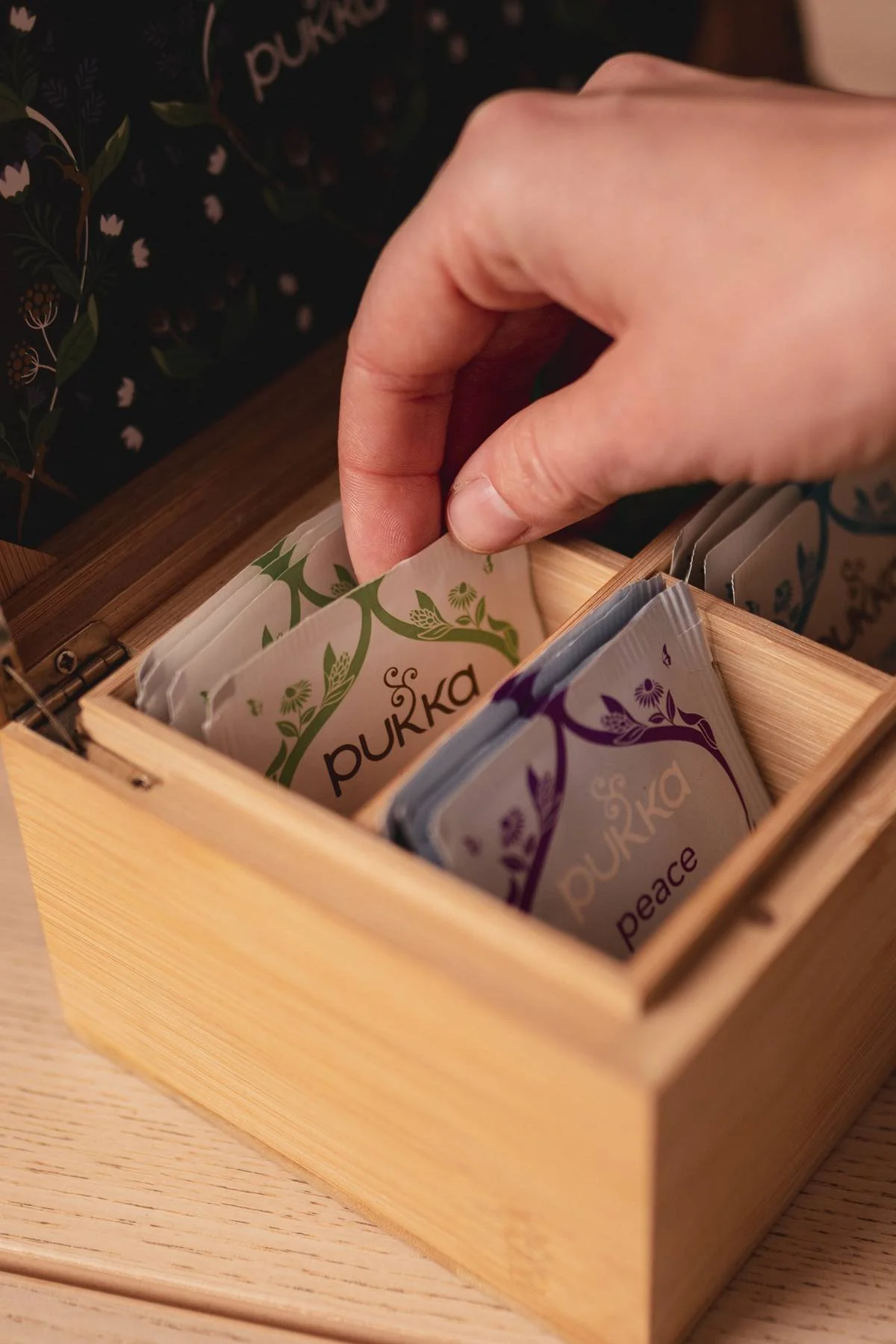 A hand reaching into a wooden box filled with tea bags labeled "pukka" and "peace." At a Kenilworth yoga studio.