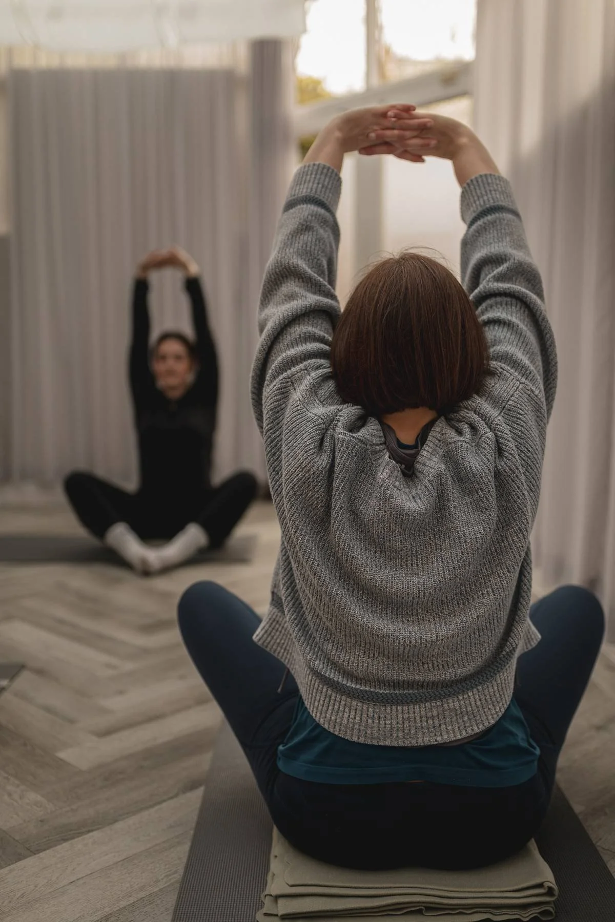 Two women sitting on yoga mats practicing stretching exercises, at The Basement Snug Yoga Studio in Kenilworth.