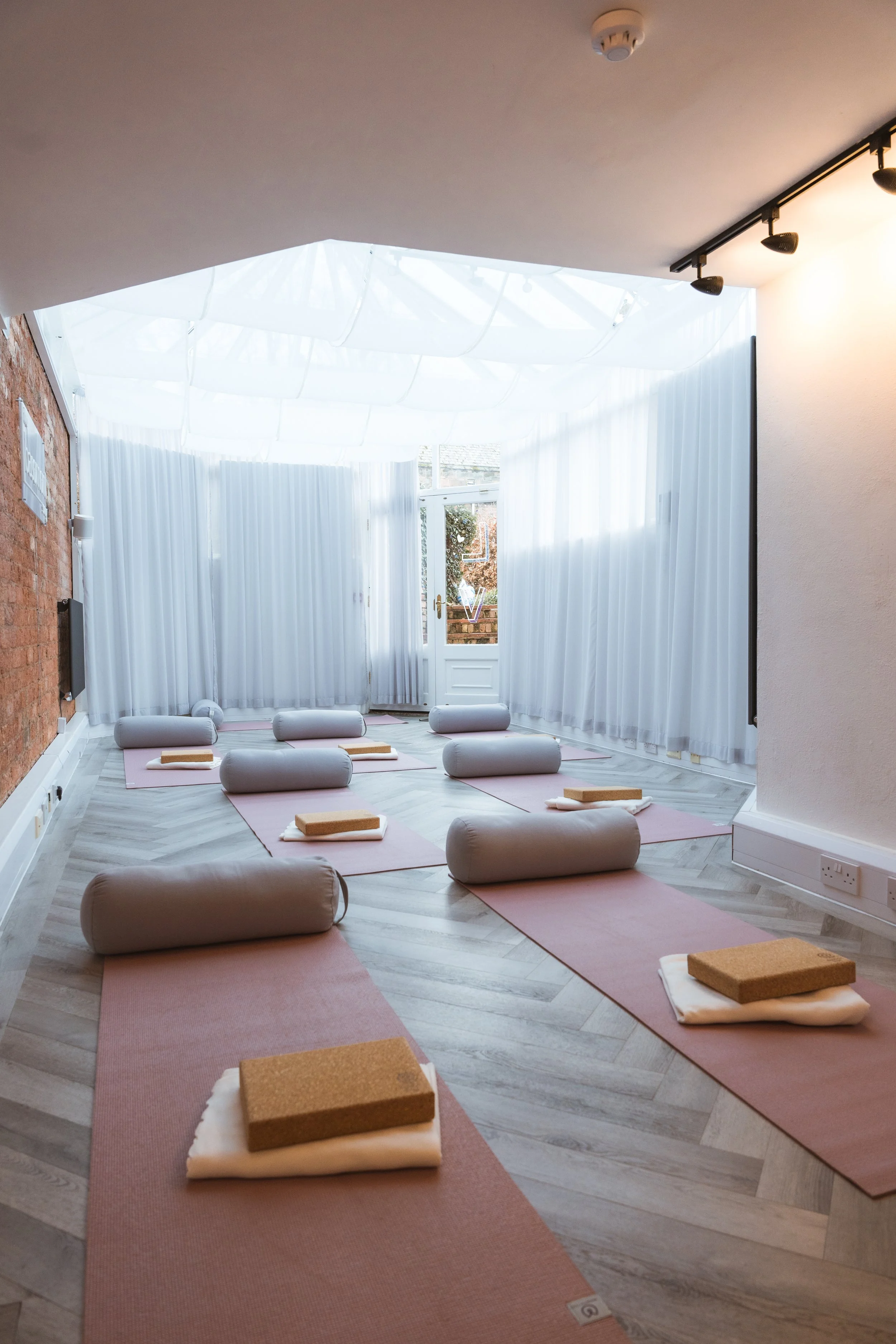 A bright, peaceful yoga studio in Kenilworth with pink mats, bolsters, blocks, and white towels aligned on the floor.