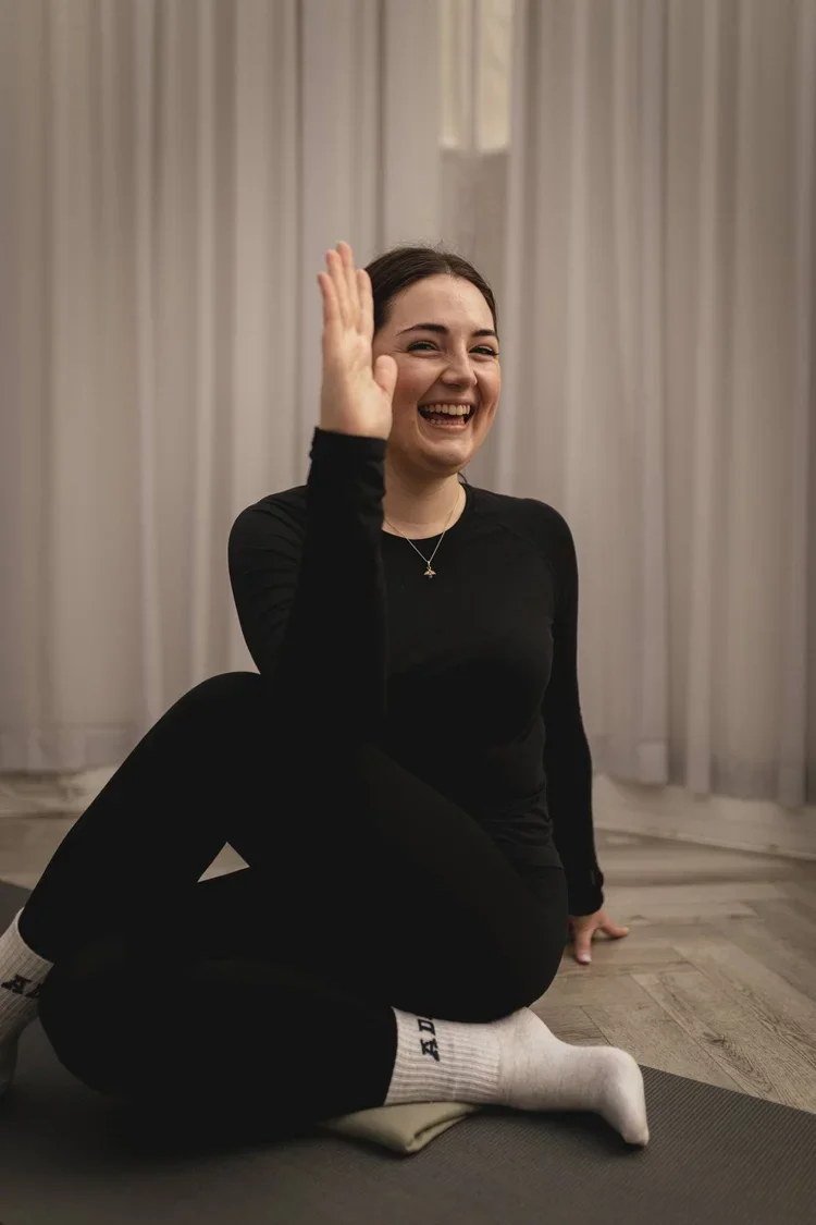 A young woman in black athletic clothing, sitting on a yoga mat at The Basement Snug Yoga Studio in Kenilworth.