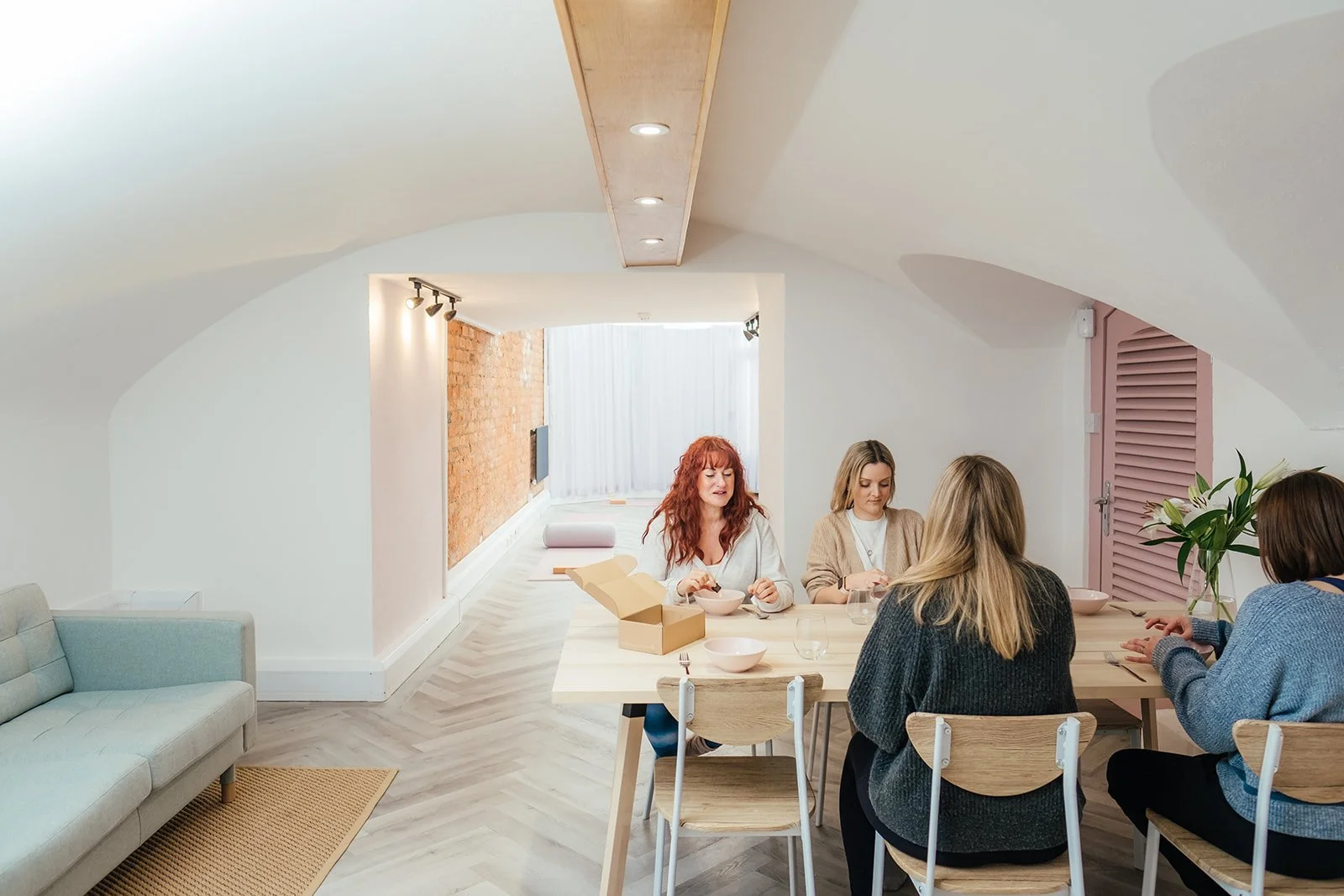 Five women sitting at a dining table in a modern, bright apartment, eating and drinking at The Basement Snug Yoga Studio in Kenilworth.