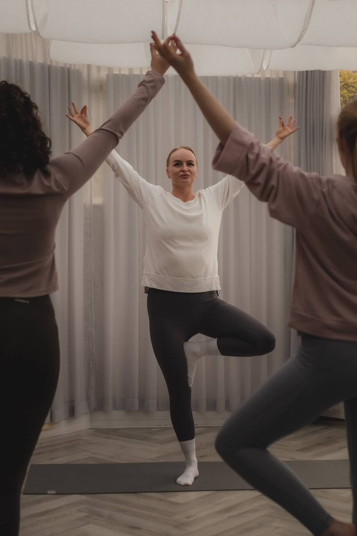 Women practicing yoga indoors, with one woman in a tree pose and two others in the foreground in some yoga poses at The Basement Snug Yoga Studio.