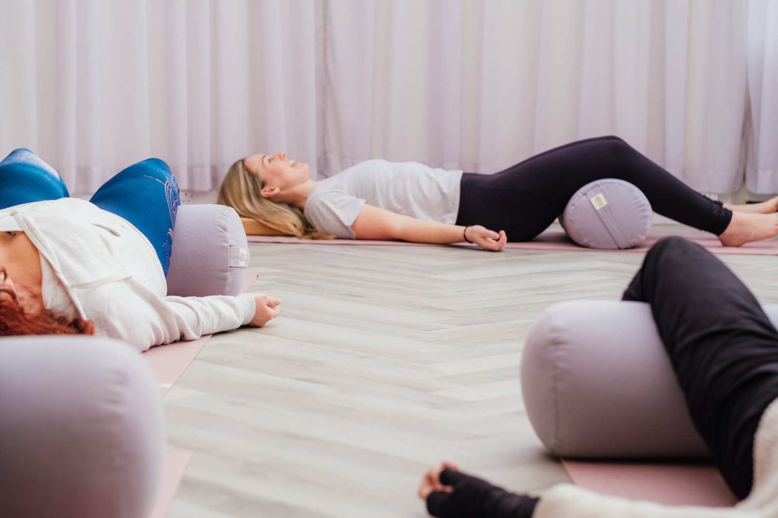 People lying on yoga mats with foam rollers underneath their knees in a yoga class at The Basement Snug Yoga Studio in Kenilworth.