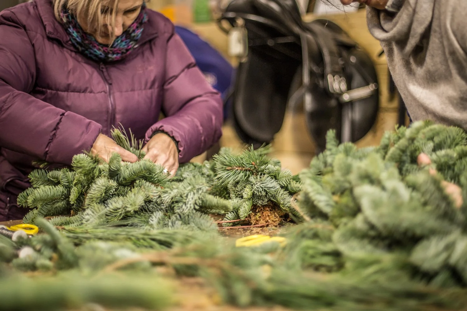 Two people working on assembling or arranging Christmas greenery or wreaths with pine branches in a workshop or store.