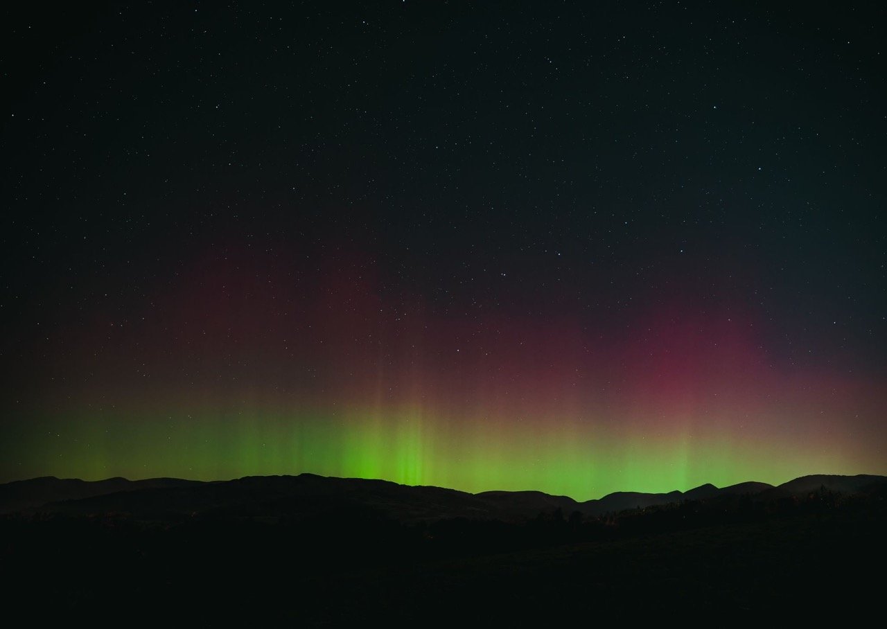 Night sky with stars and the northern lights over a silhouette of mountains.