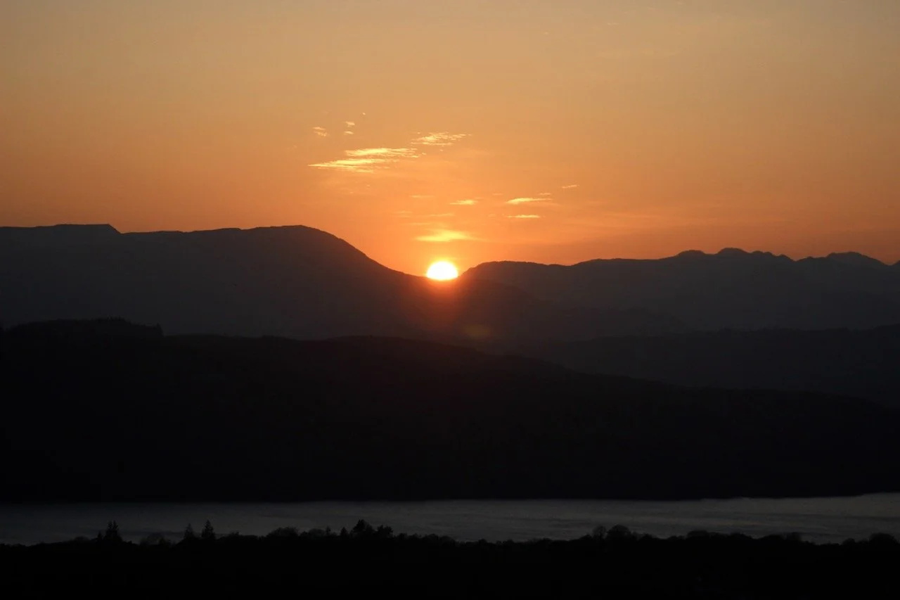 Sunset over mountain range with orange sky and silhouetted hills