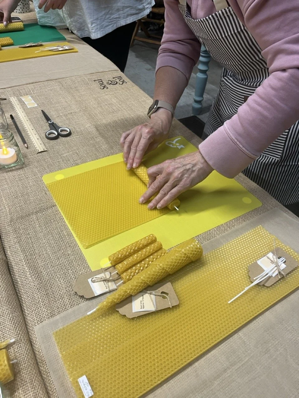 Person demonstrating beeswax candle rolling on a yellow cutting mat at a craft workshop.