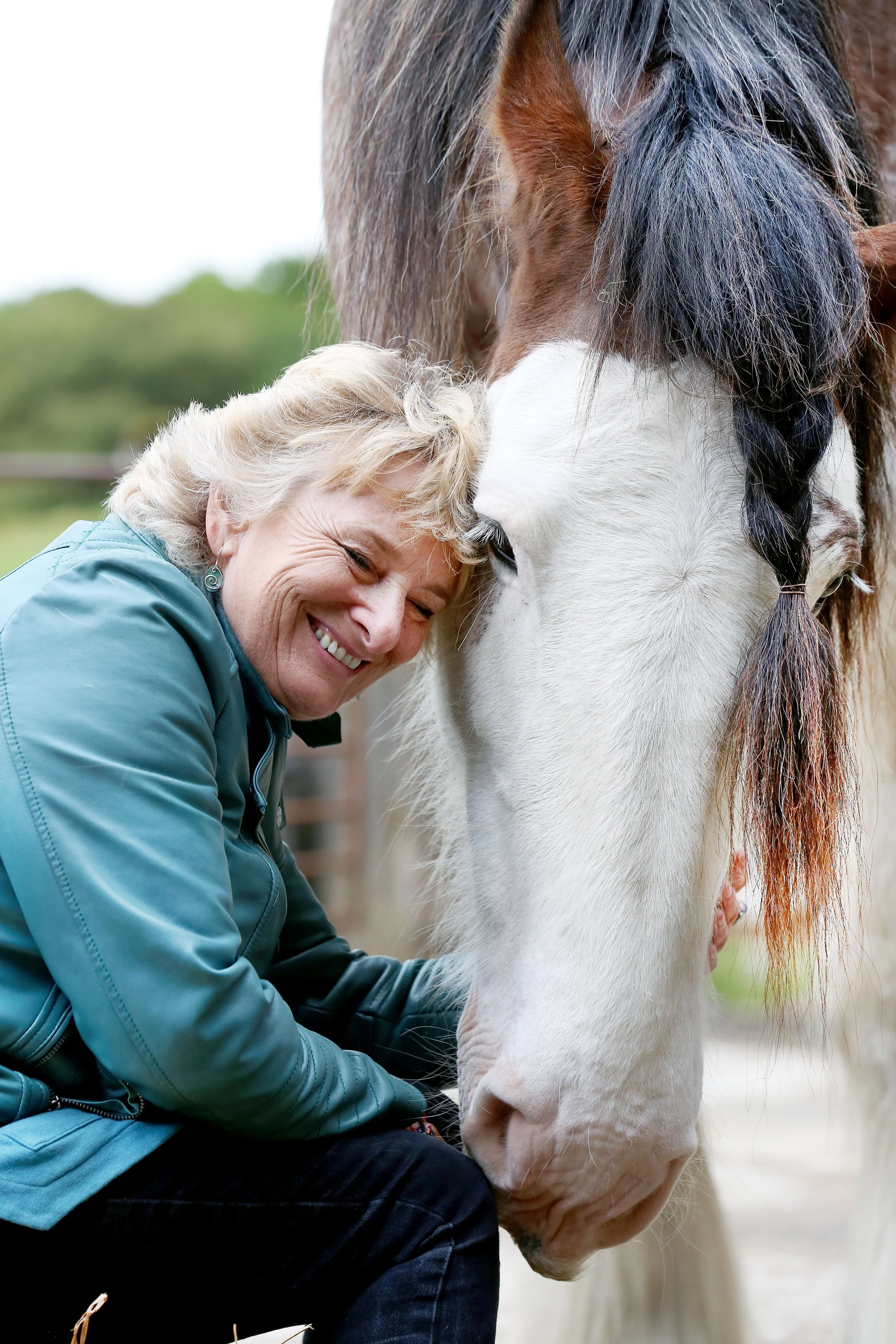 A woman hugging a white horse with brown markings, smiling and enjoying the moment outdoors.