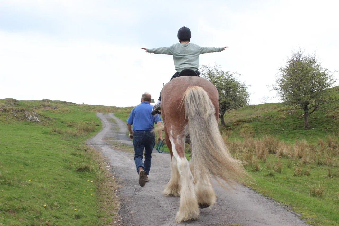Child wearing helmet riding a horse on a country trail, with two adults walking nearby.