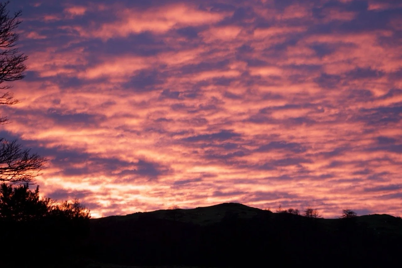 A vibrant sunset with pink and orange clouds over silhouetted hills and trees.