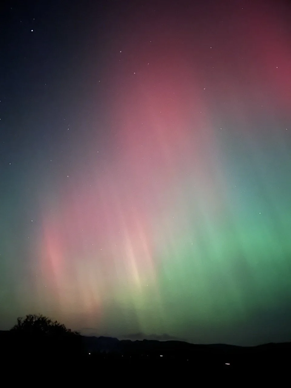 Night sky displaying colorful aurora borealis in shades of pink, green, and purple, with stars visible above dark silhouette of landscape.