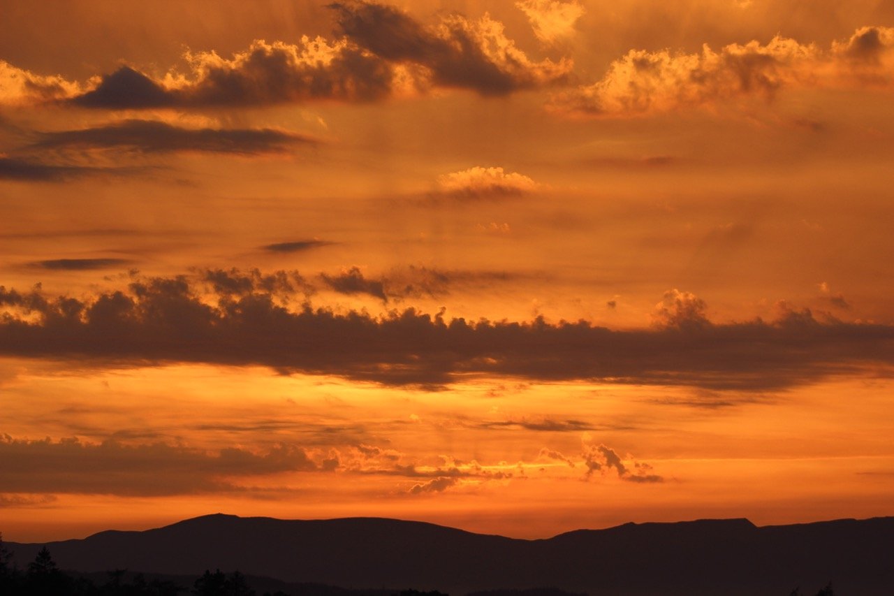 A vibrant sunset over a mountain range, with orange and gold hues illuminating the sky and clouds.